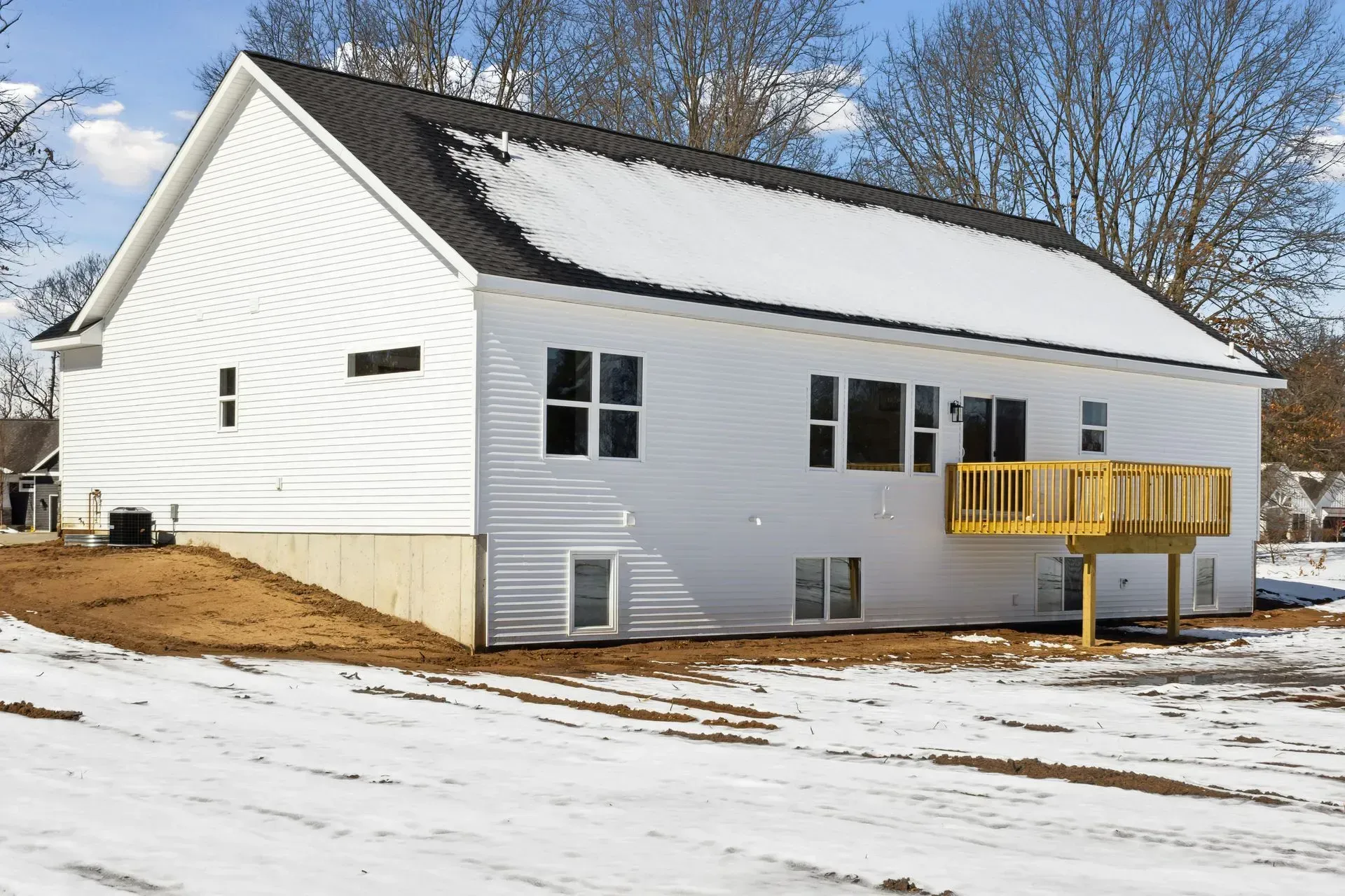 Snow-covered white house with a yellow deck under a clear winter sky