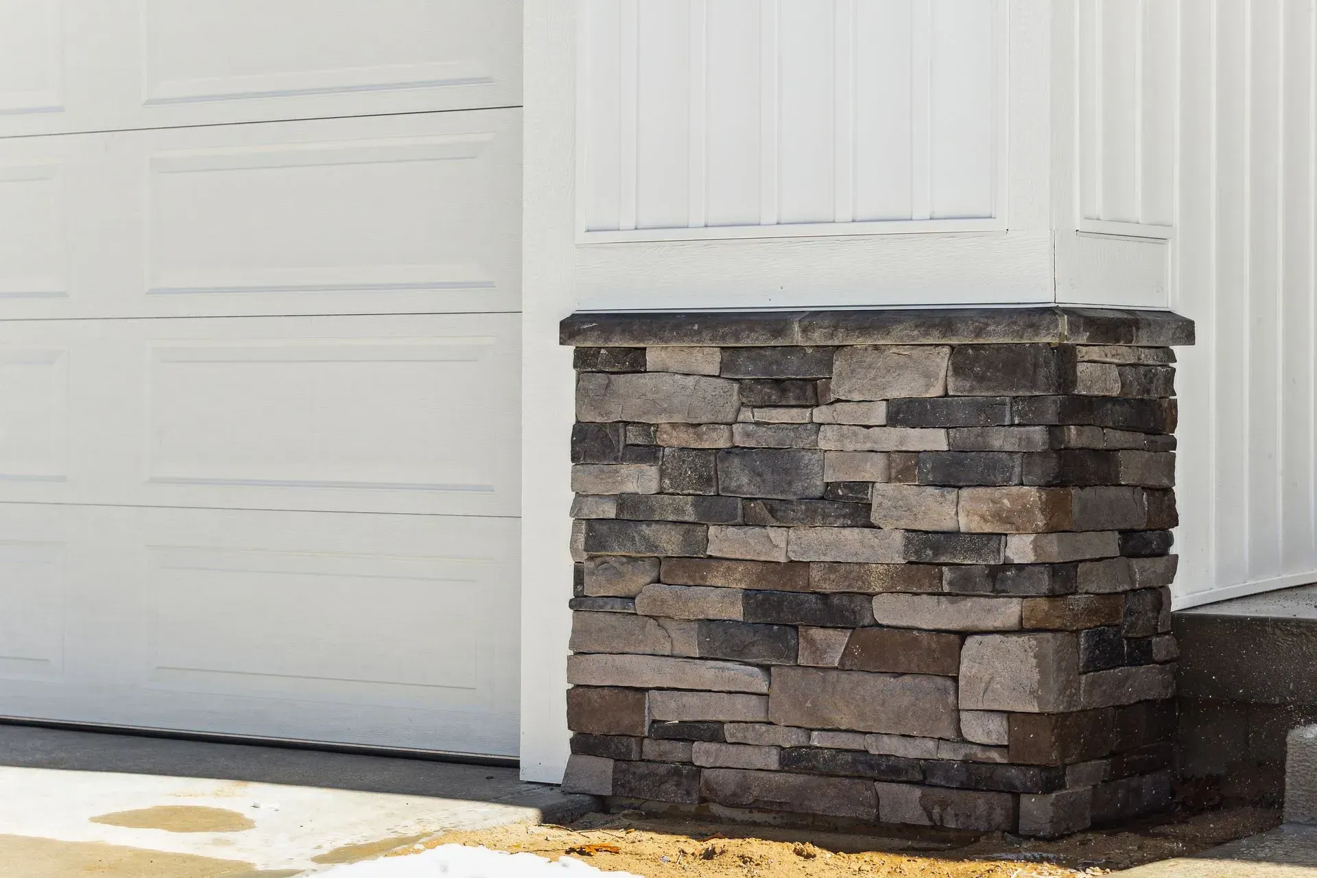 White garage door beside a stone-faced porch column and step in daylight