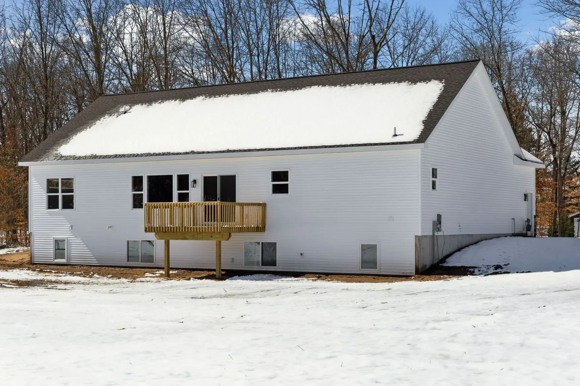 Snow-covered white house with a small wooden front porch and bare trees behind it.