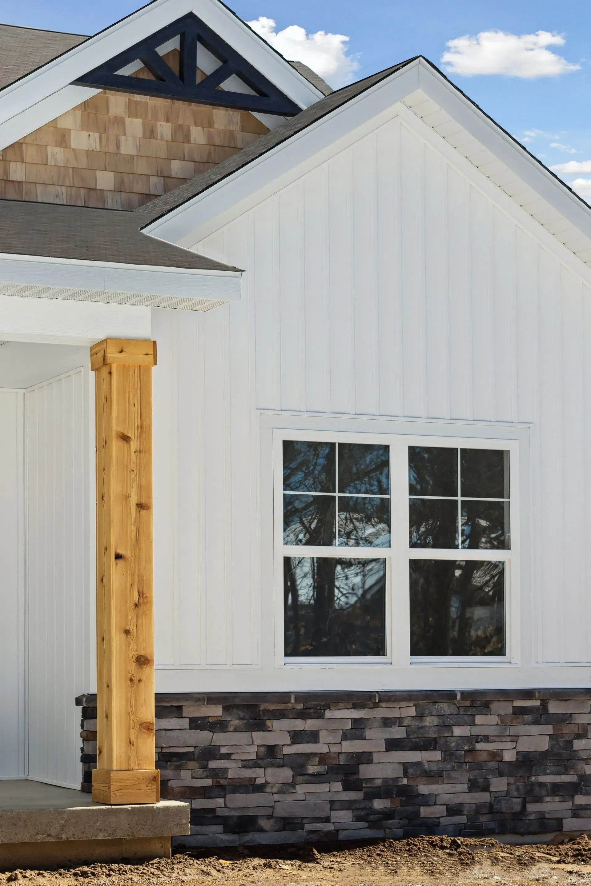 White house exterior with gabled roof, window, stone base, and wood front post