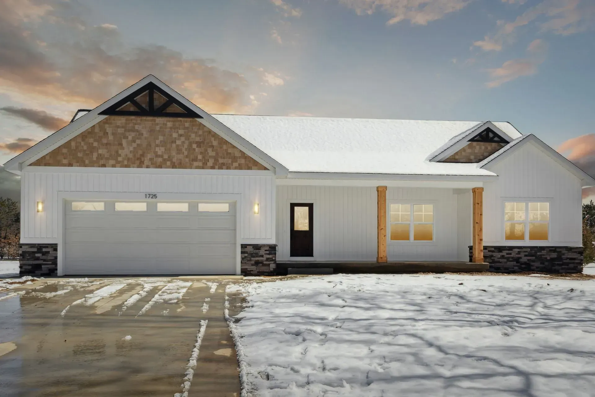 Snow-covered modern house with a two-car garage at sunset