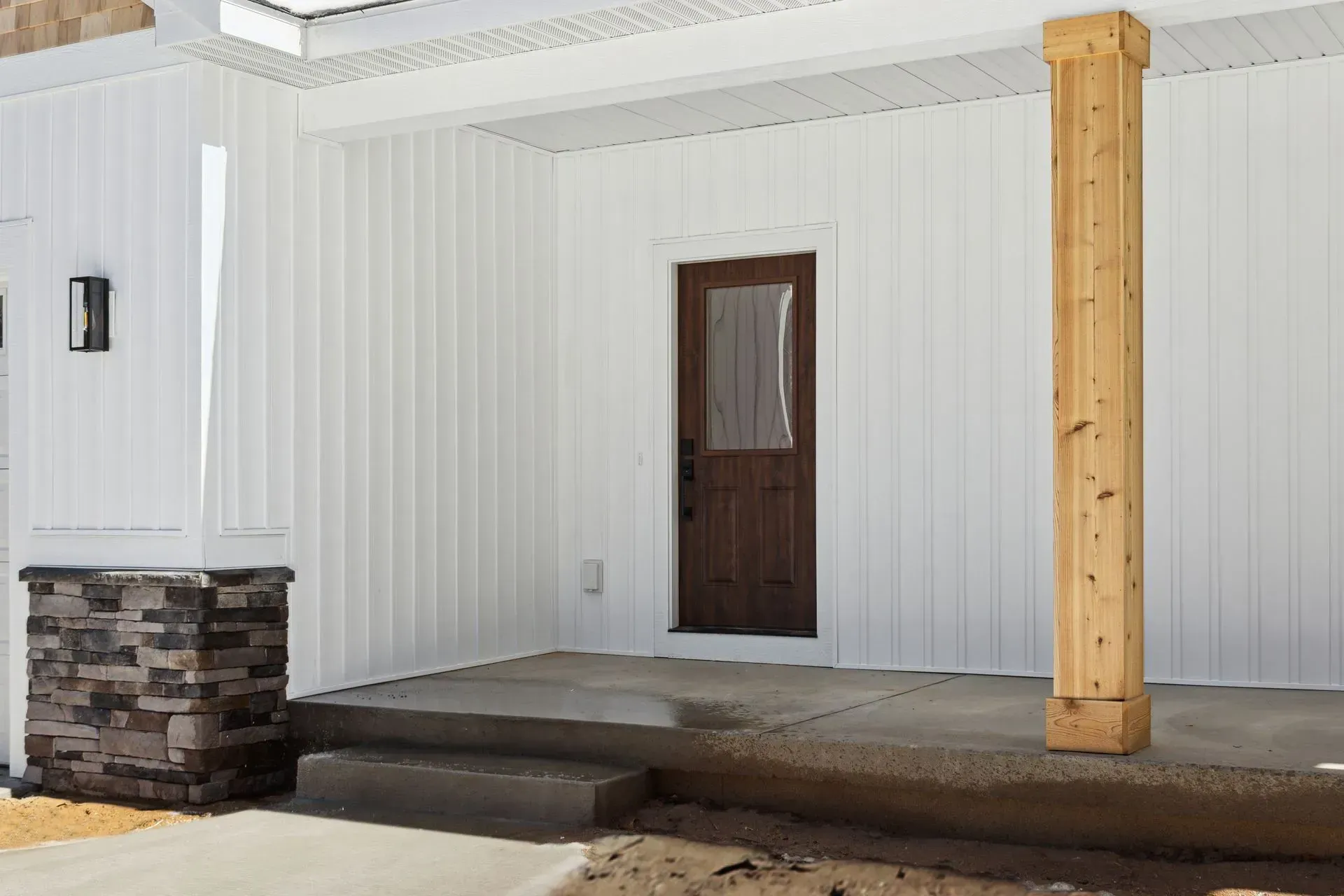 Covered porch with white siding, stone steps, and a dark wooden door beside a timber post