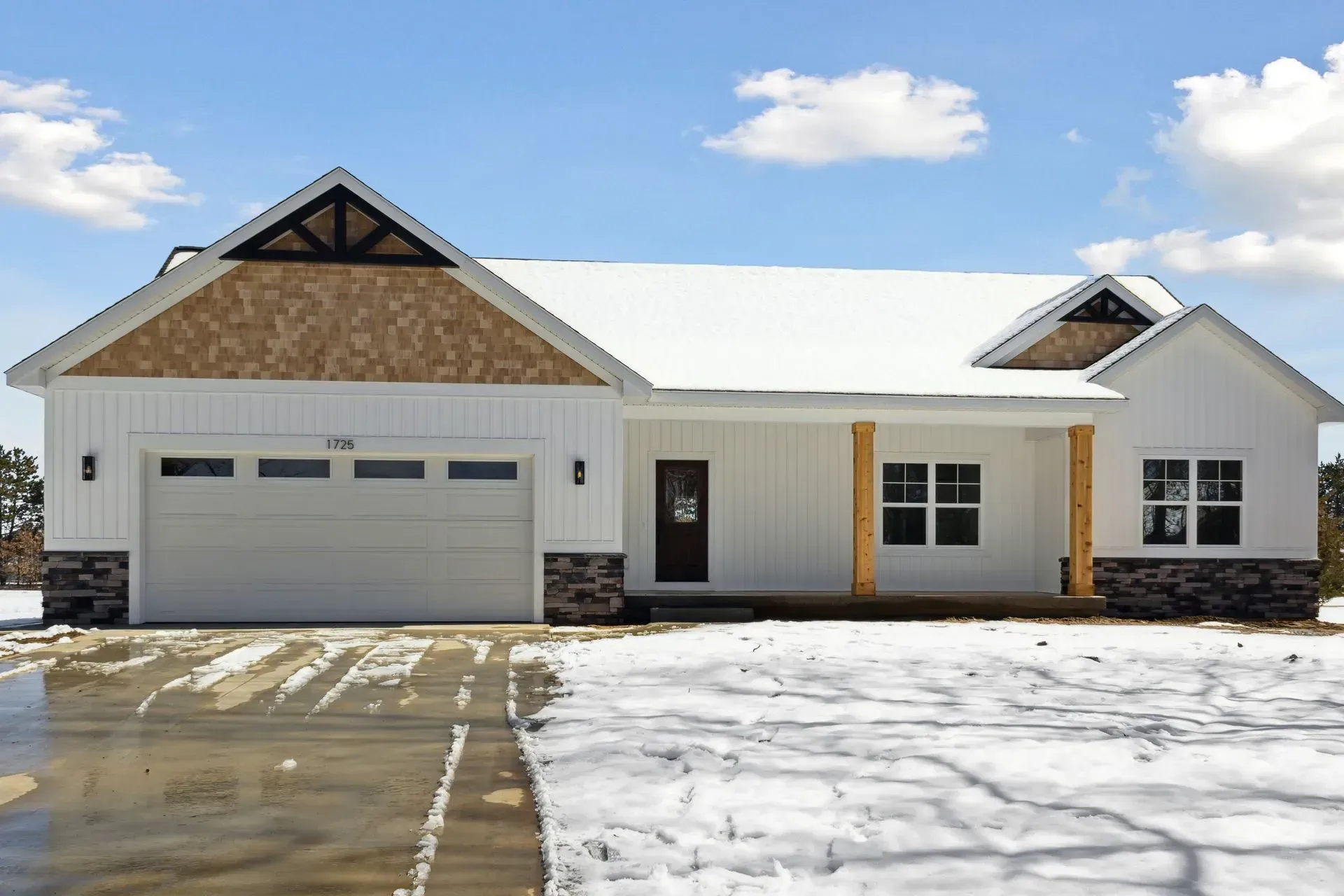 Snow-covered modern house with a two-car garage and white exterior under a blue sky