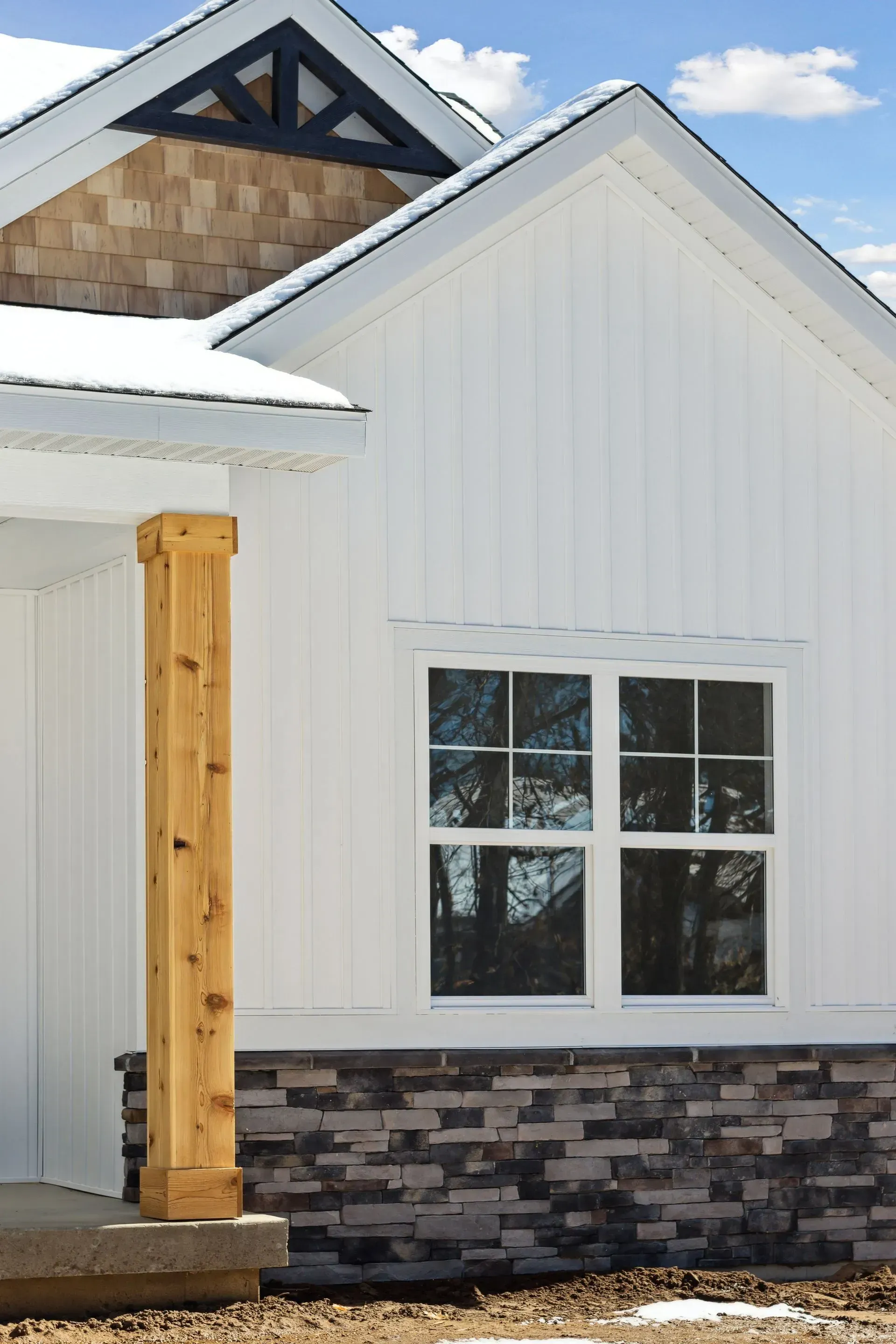 White house exterior with gabled roof, stone base, wooden post, and a window under a blue sky