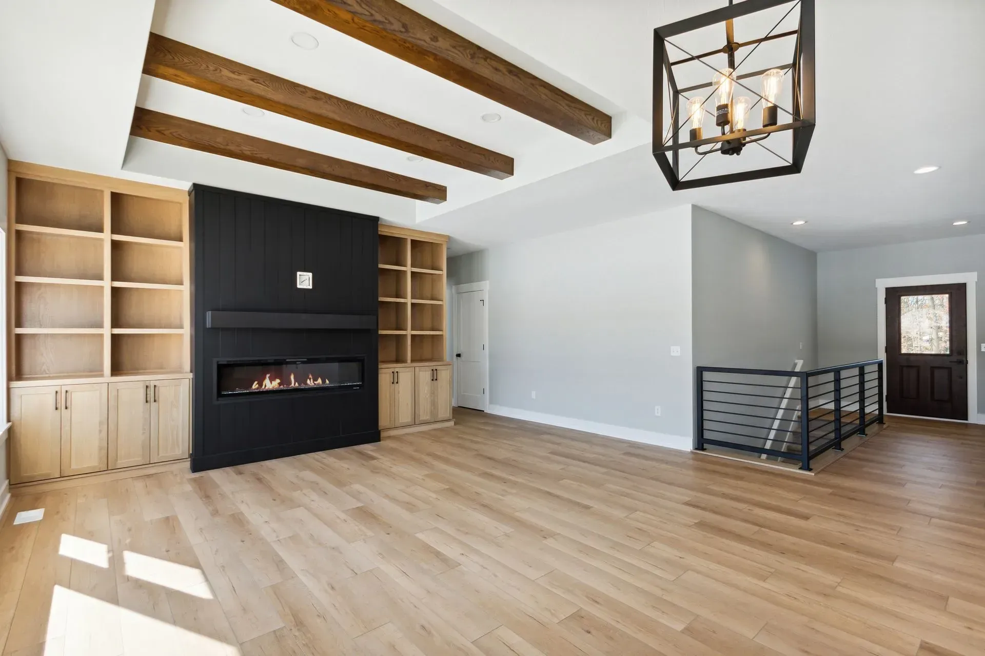 Bright living room with hardwood floors, exposed beams, built-in shelves, and a modern black fireplace.