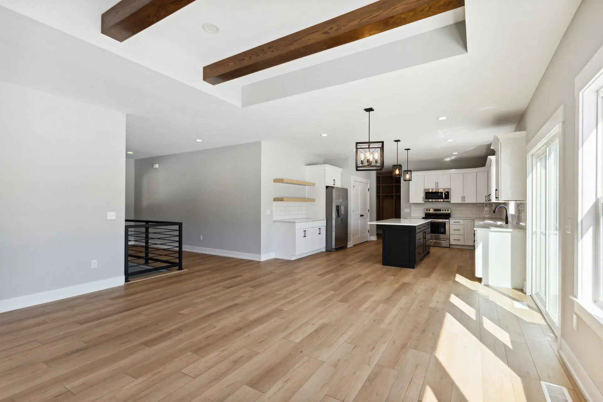 Open-concept kitchen and living room with wood floors, exposed beams, and large sunlit windows