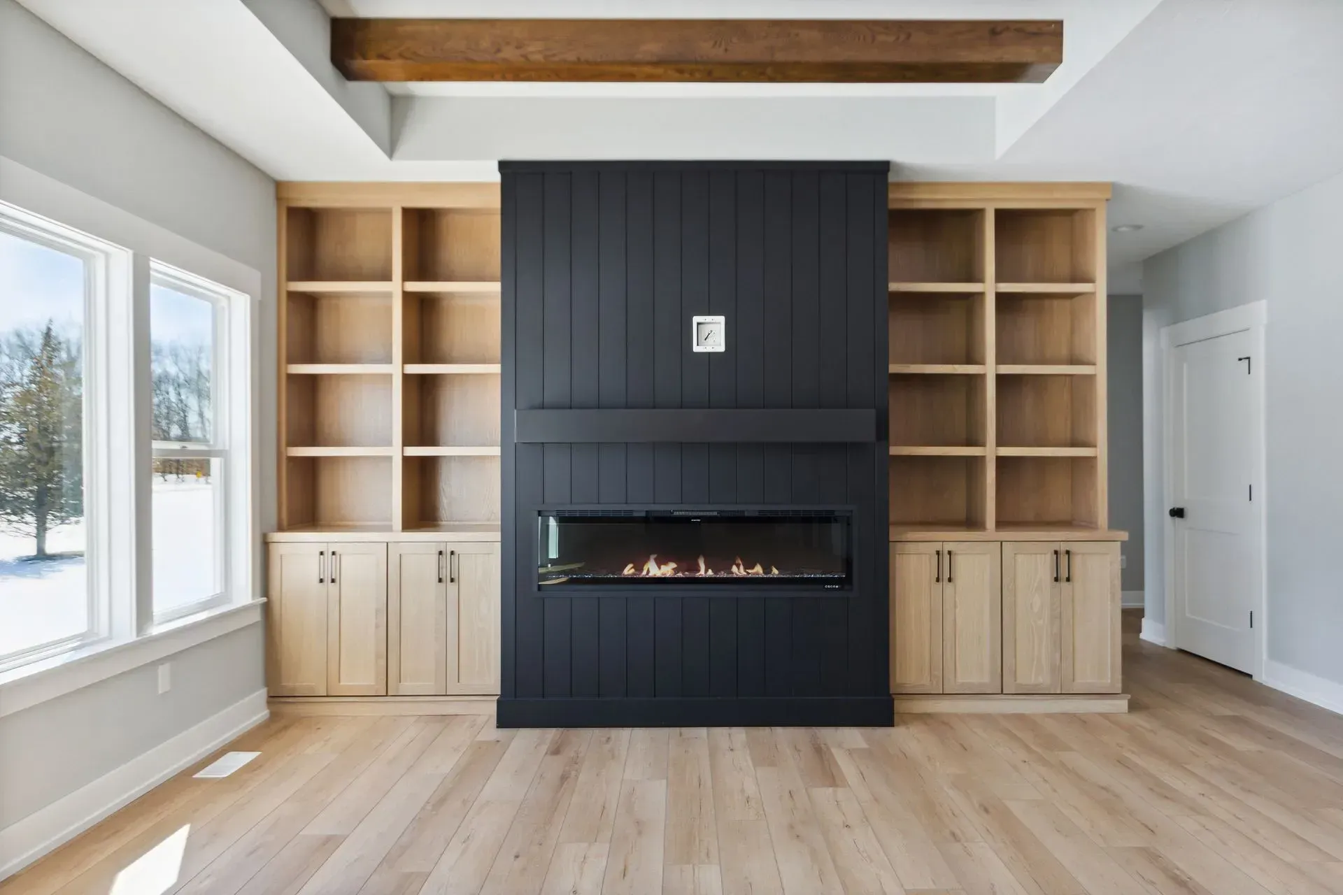 Modern living room with built-in shelves, dark fireplace center, light wood cabinets, and large windows