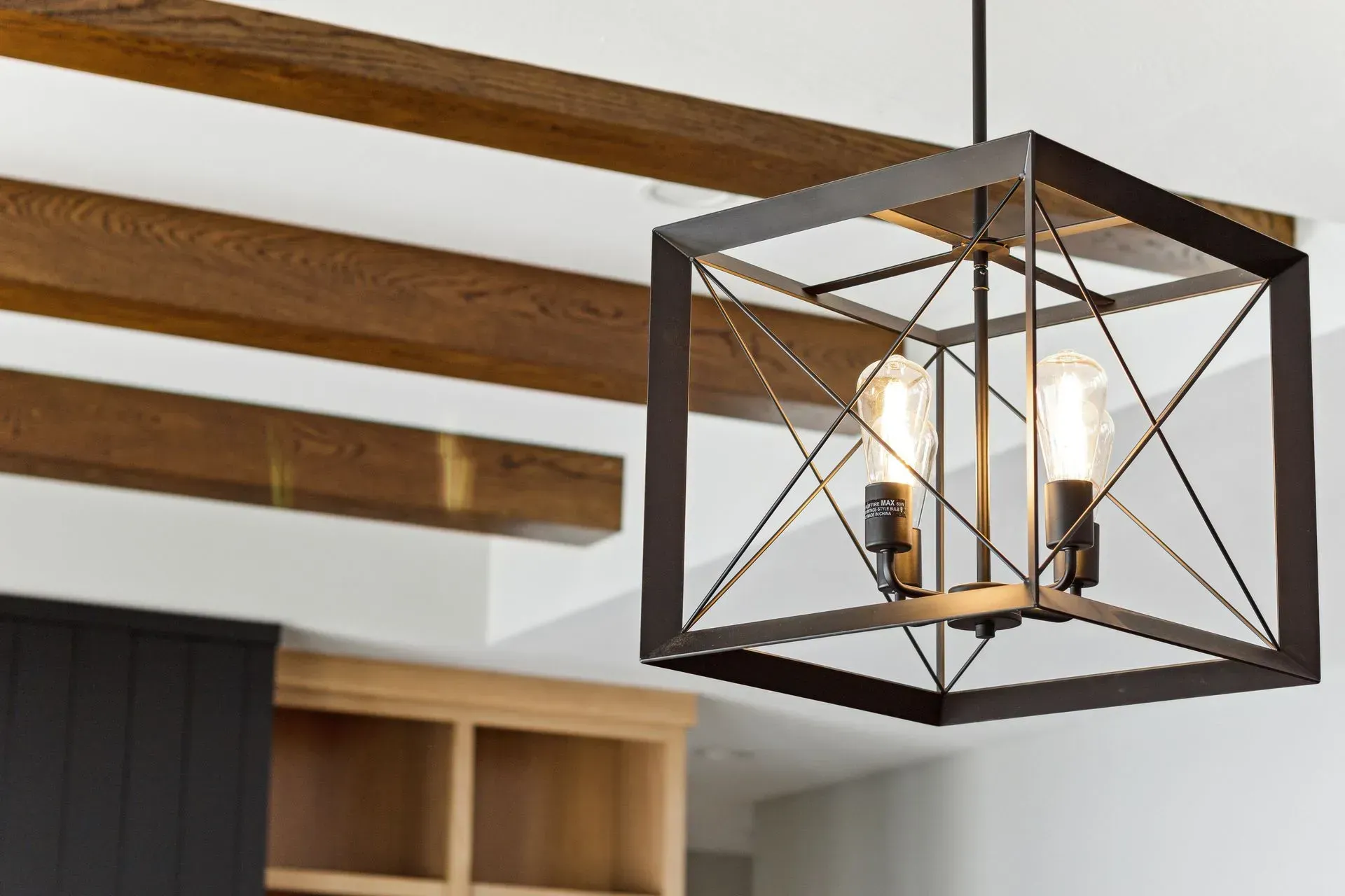 Black metal geometric pendant light with exposed bulbs hanging from a wood-beamed ceiling