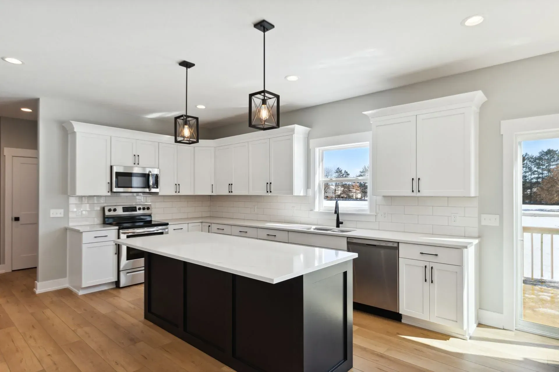Bright modern kitchen with white cabinets, black island, pendant lights, and hardwood floors