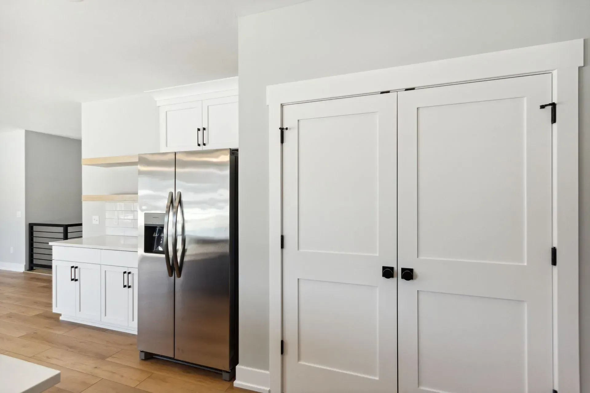 Bright modern kitchen with white cabinets, stainless steel fridge, and double pantry doors