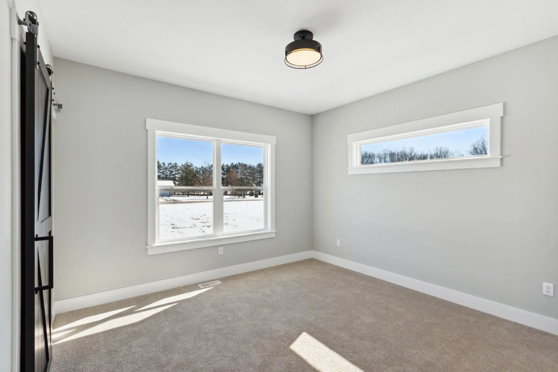 Empty beige bedroom with gray walls, carpet, and two windows letting in bright winter light.