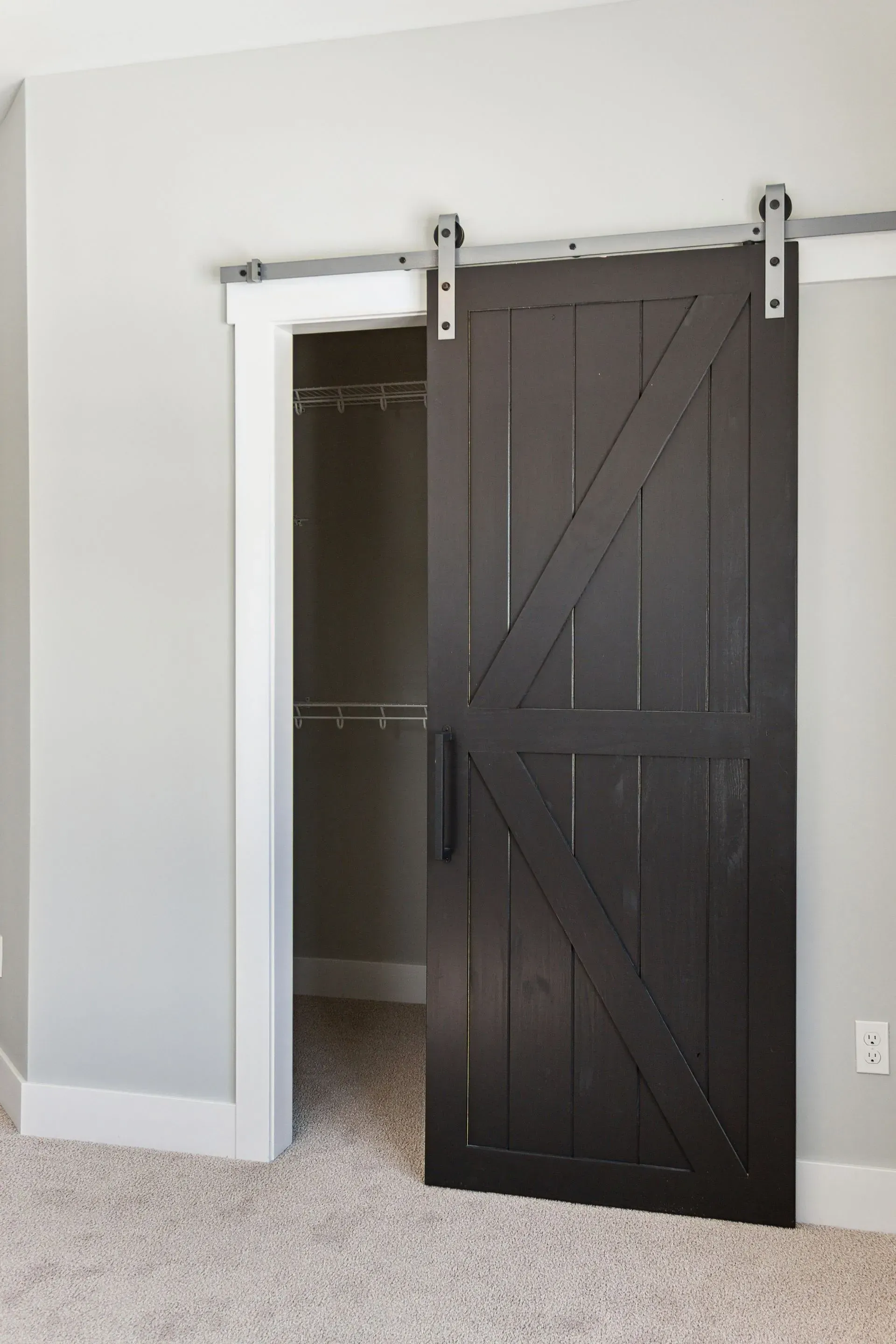 Dark barn door partly open on a closet in a beige-carpeted room