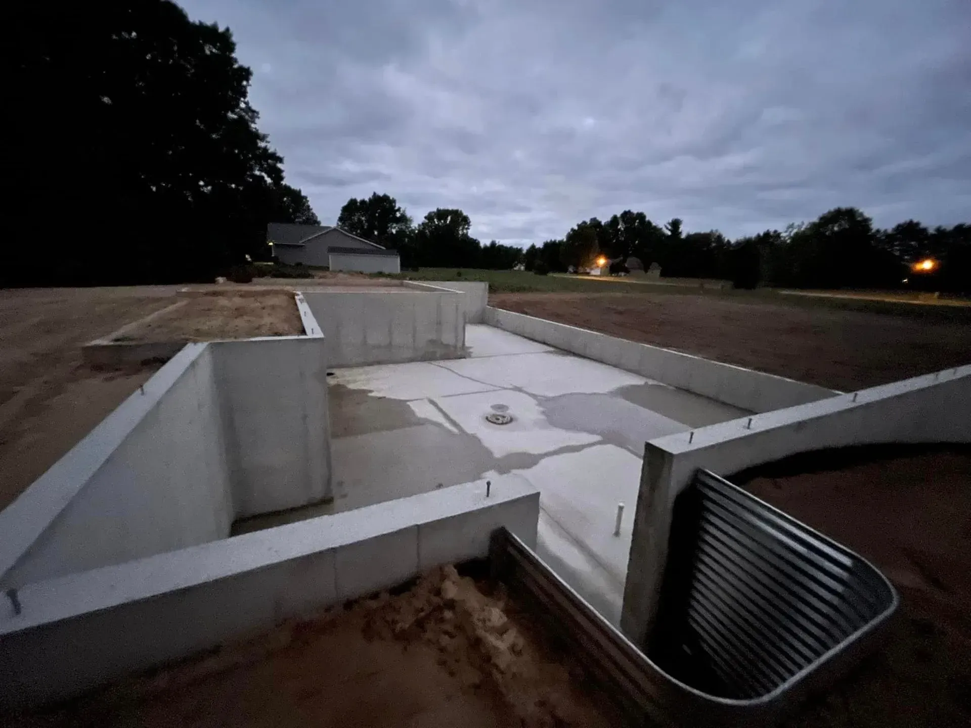 Concrete drainage channel at dusk with white retaining walls and a metal grate in the foreground
