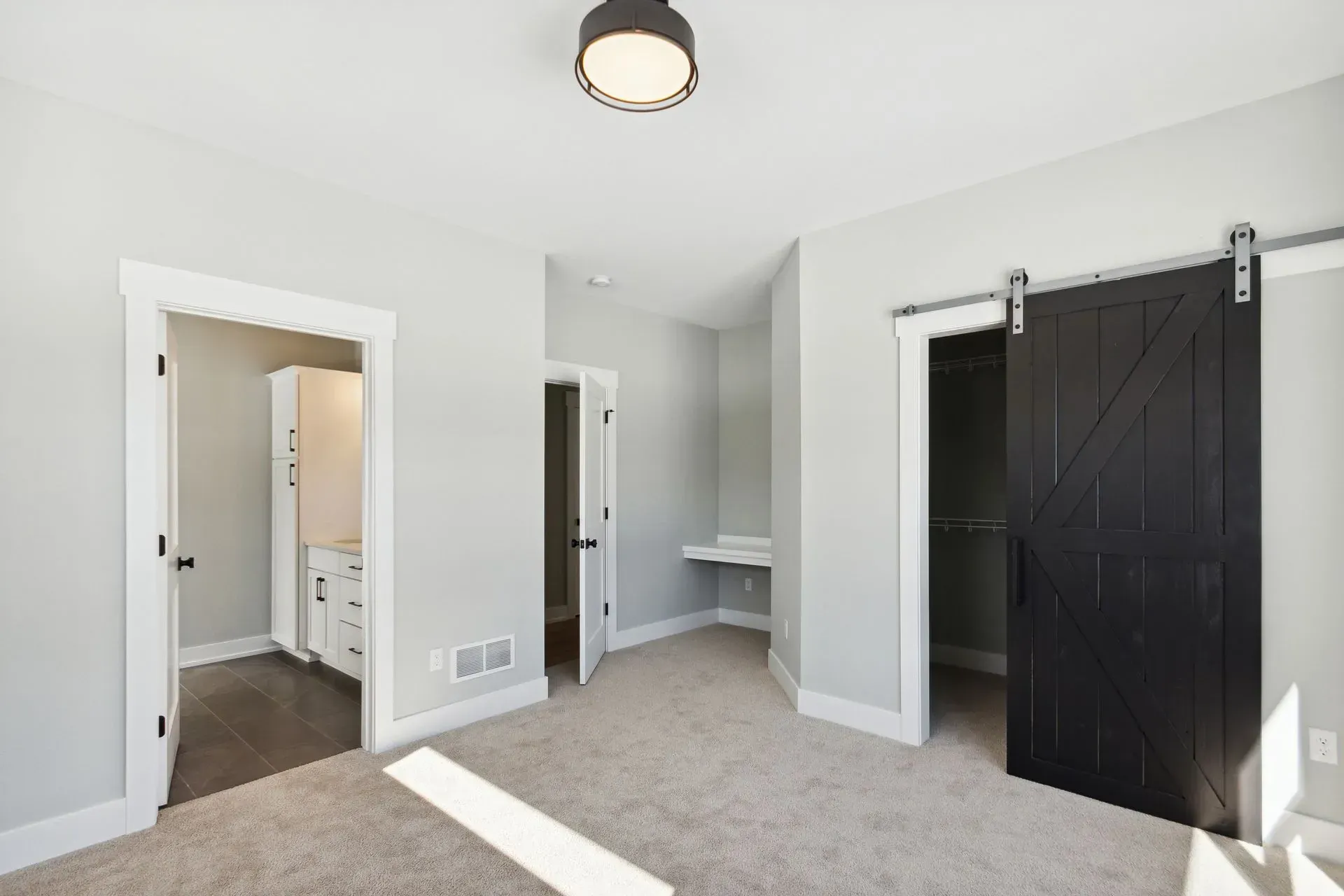 Bright bedroom with beige carpet, white walls, open doors, and a black sliding barn door.