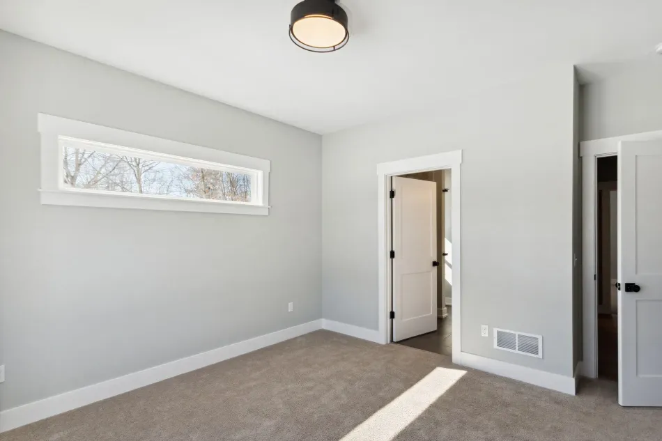 Empty gray bedroom with carpet, narrow window, and open closet and doorway.