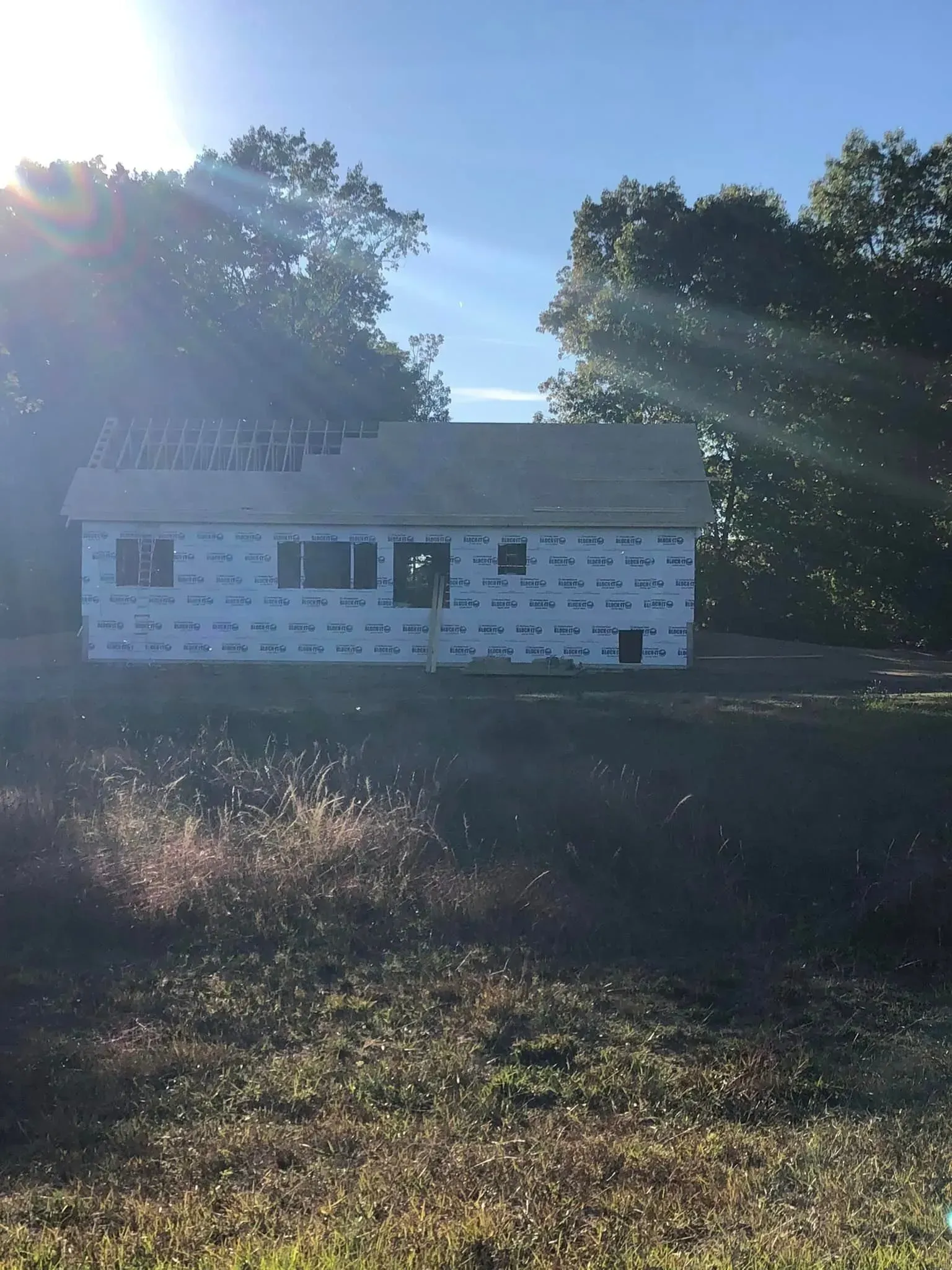 Small white house under bright sunlight, surrounded by trees and a grassy yard.