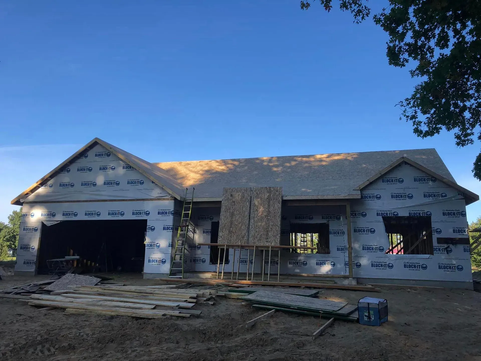 Partially built house with exposed framing, white wrap, and open garage in a suburban lot at dusk