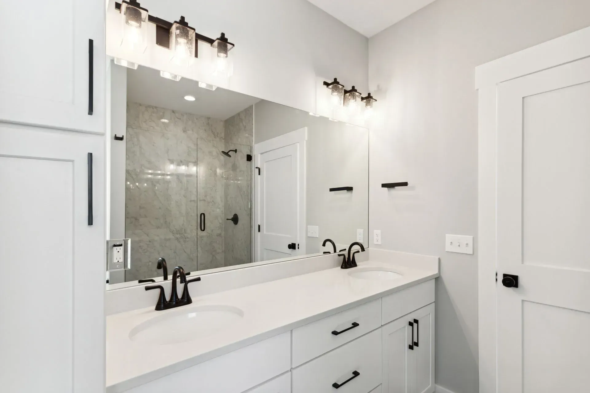 Bright white bathroom vanity with large mirror, glass shower, and modern light fixtures