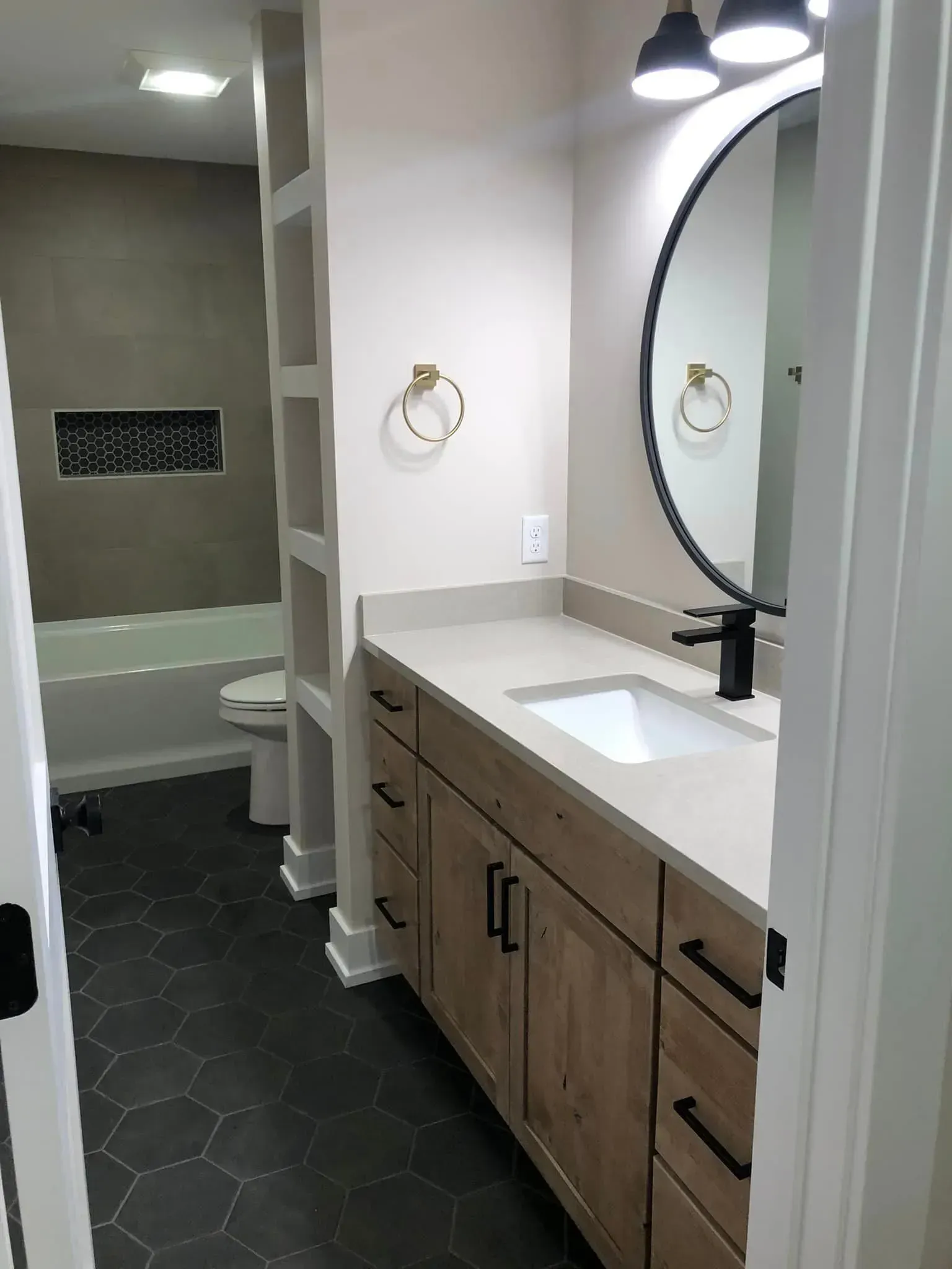 Modern bathroom vanity with wood cabinets, large round mirror, black faucet, and walk-in shower in the background