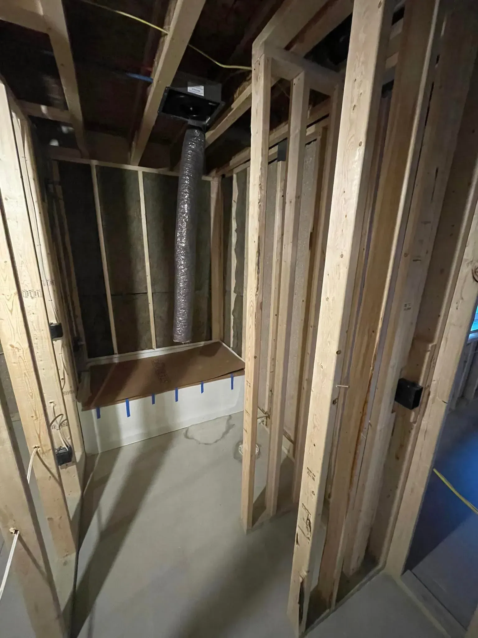 Unfinished basement framing with exposed studs, ductwork, and a small shelf or ledge along the wall.