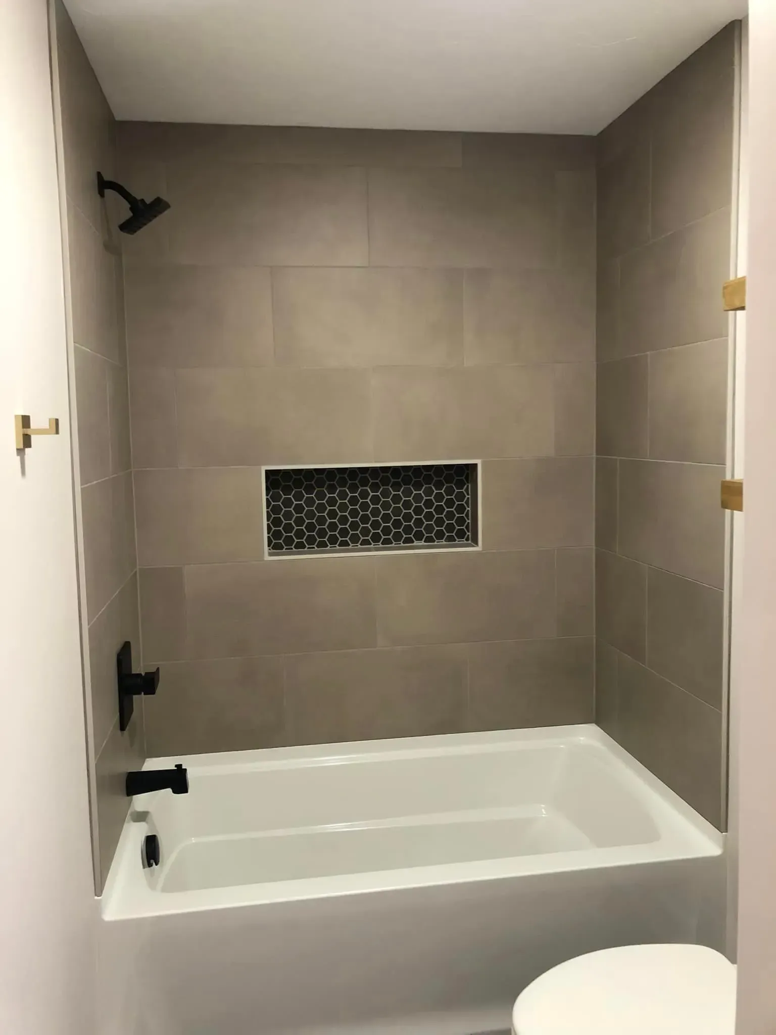 Tile-lined bathroom with a shower-tub combo and built-in recessed shelf, seen through an open door