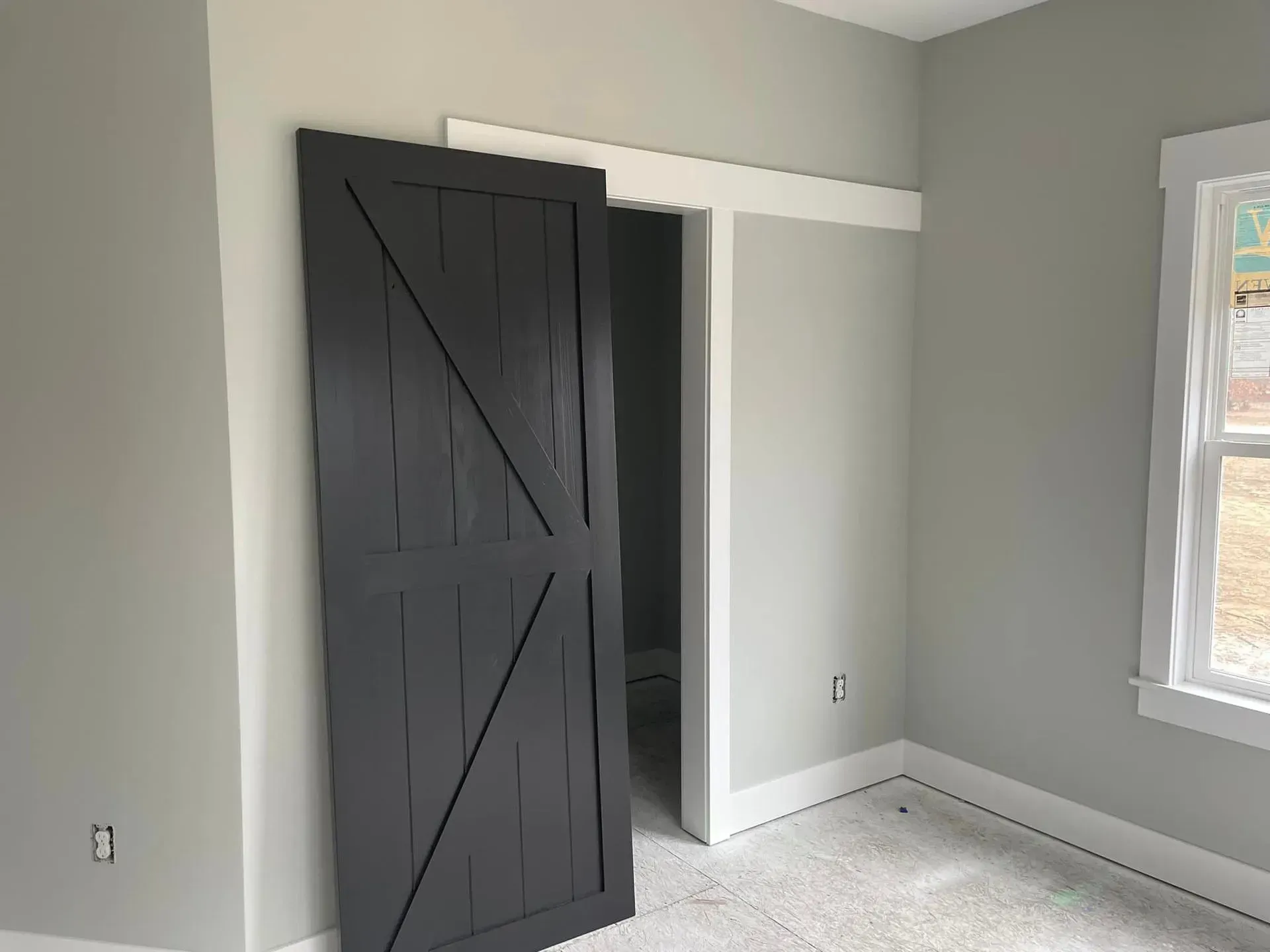 Empty room with gray walls, white trim, and a dark barn-style sliding door open to a closet.