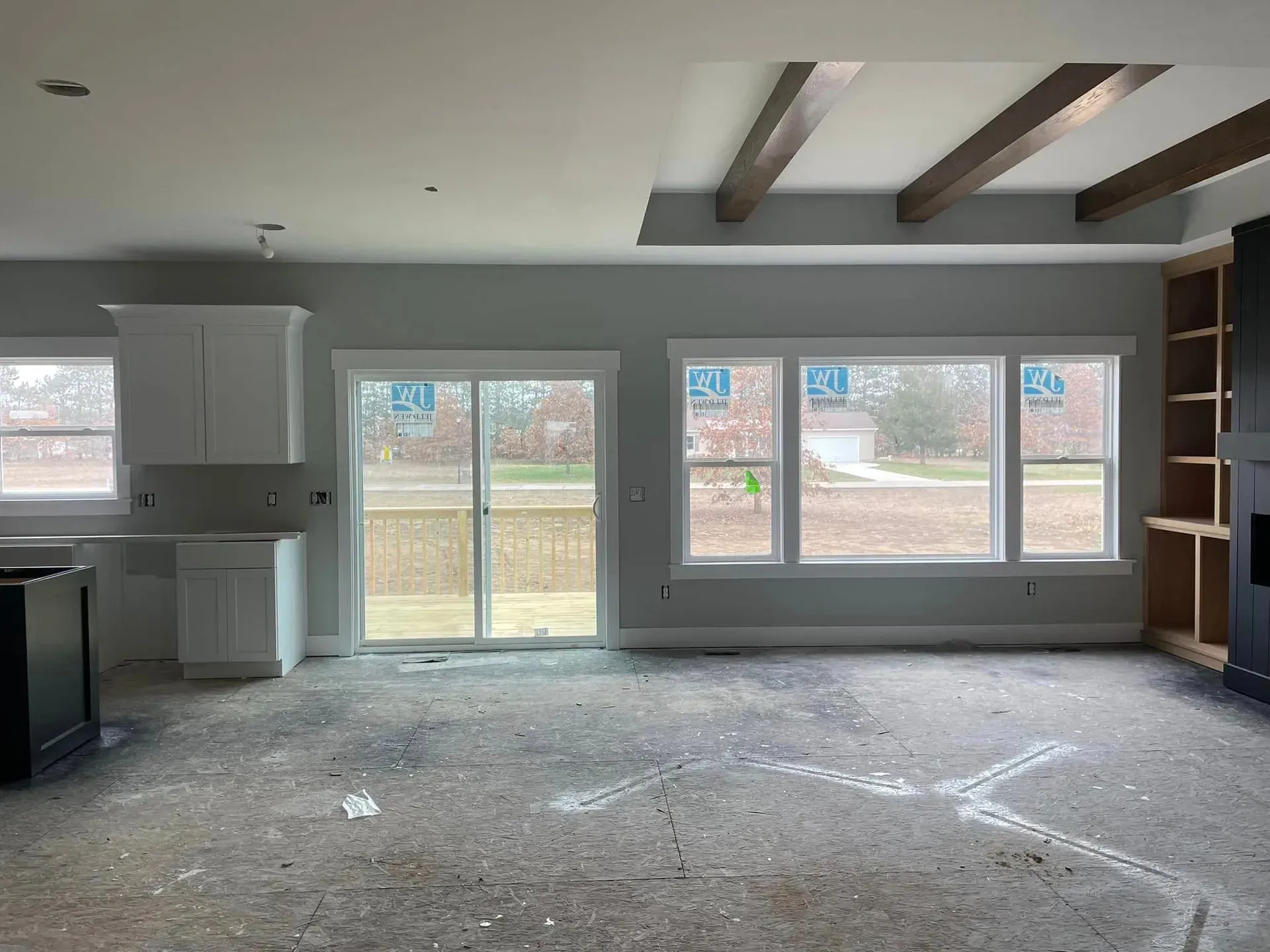 Empty living room with exposed ceiling beams, large windows, and unfinished floor.