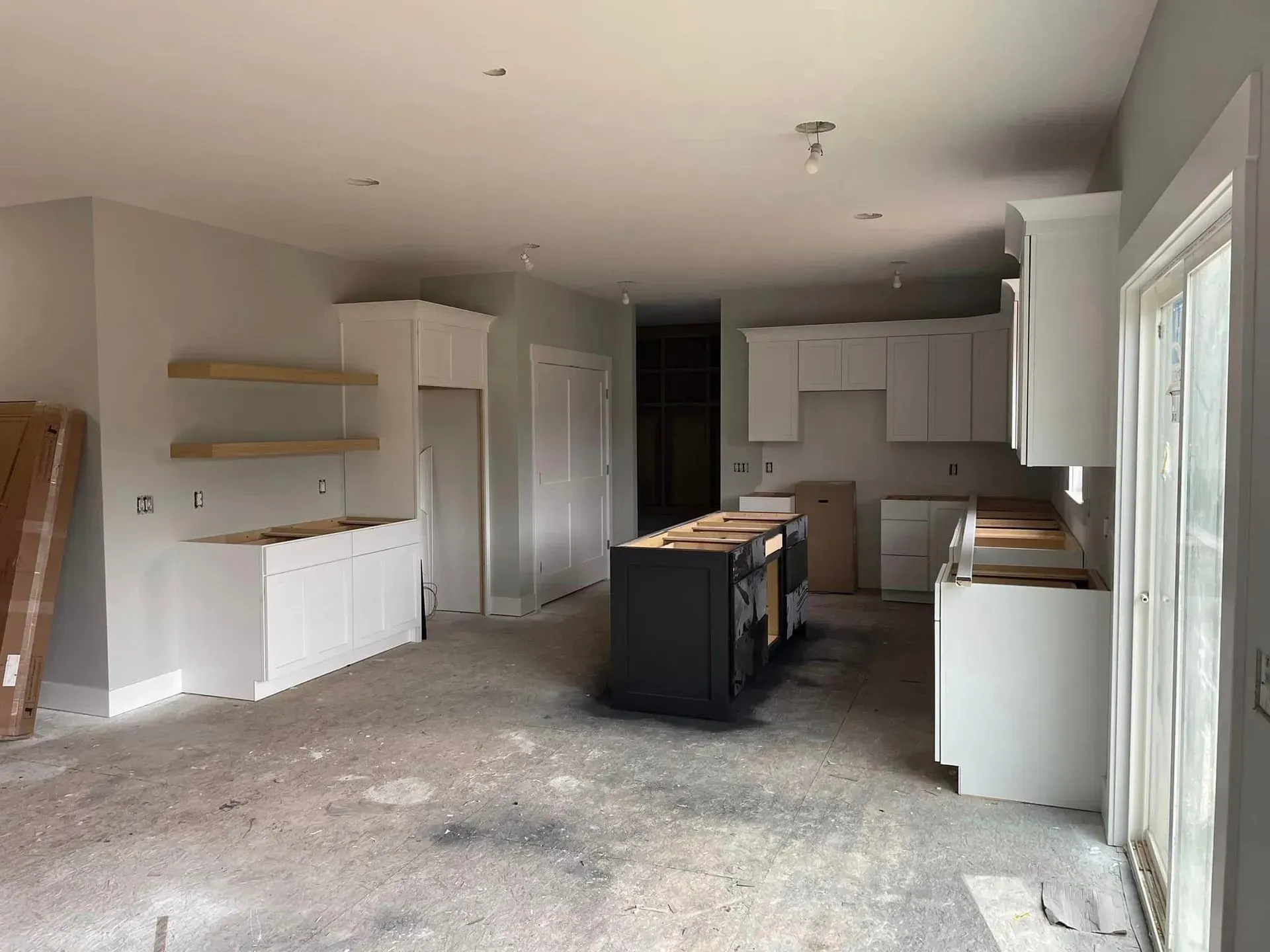 Unfinished kitchen and living area with cabinets, island, and countertops in a bright room