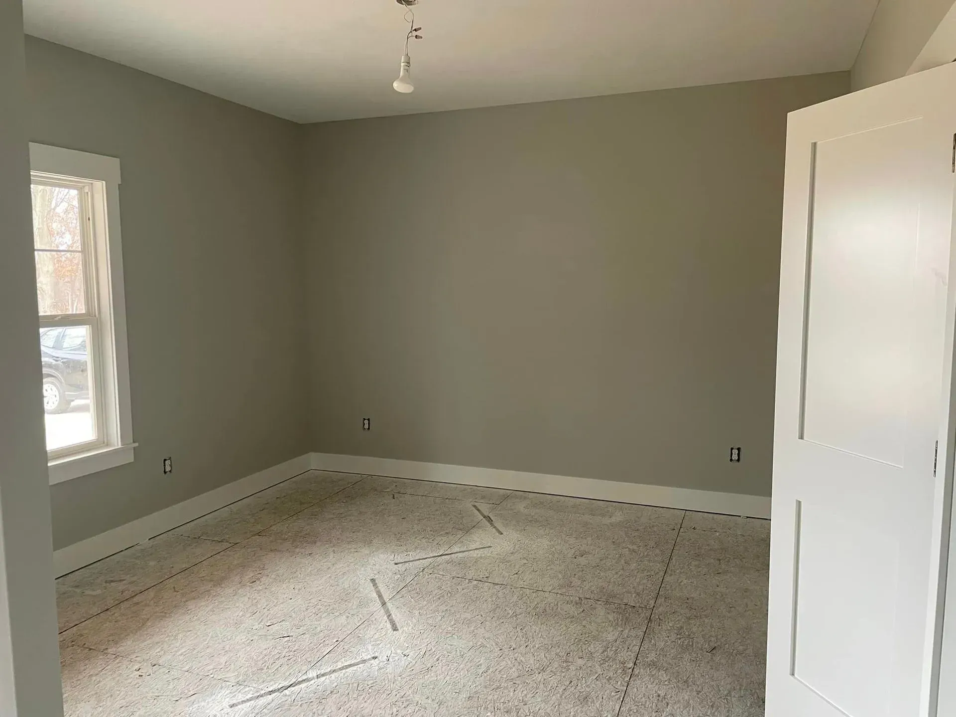Empty room with gray walls, white trim, a window, and unfinished flooring