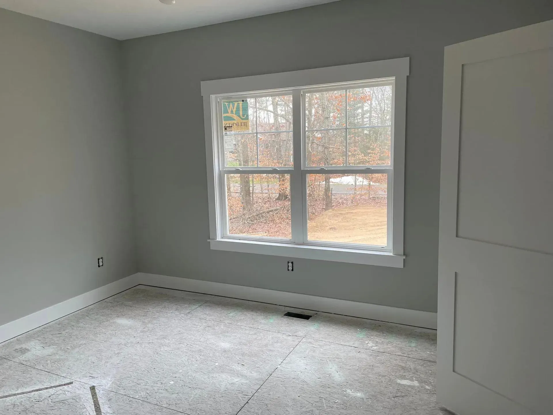 Empty gray bedroom with white trim, large window, and carpeted floor.