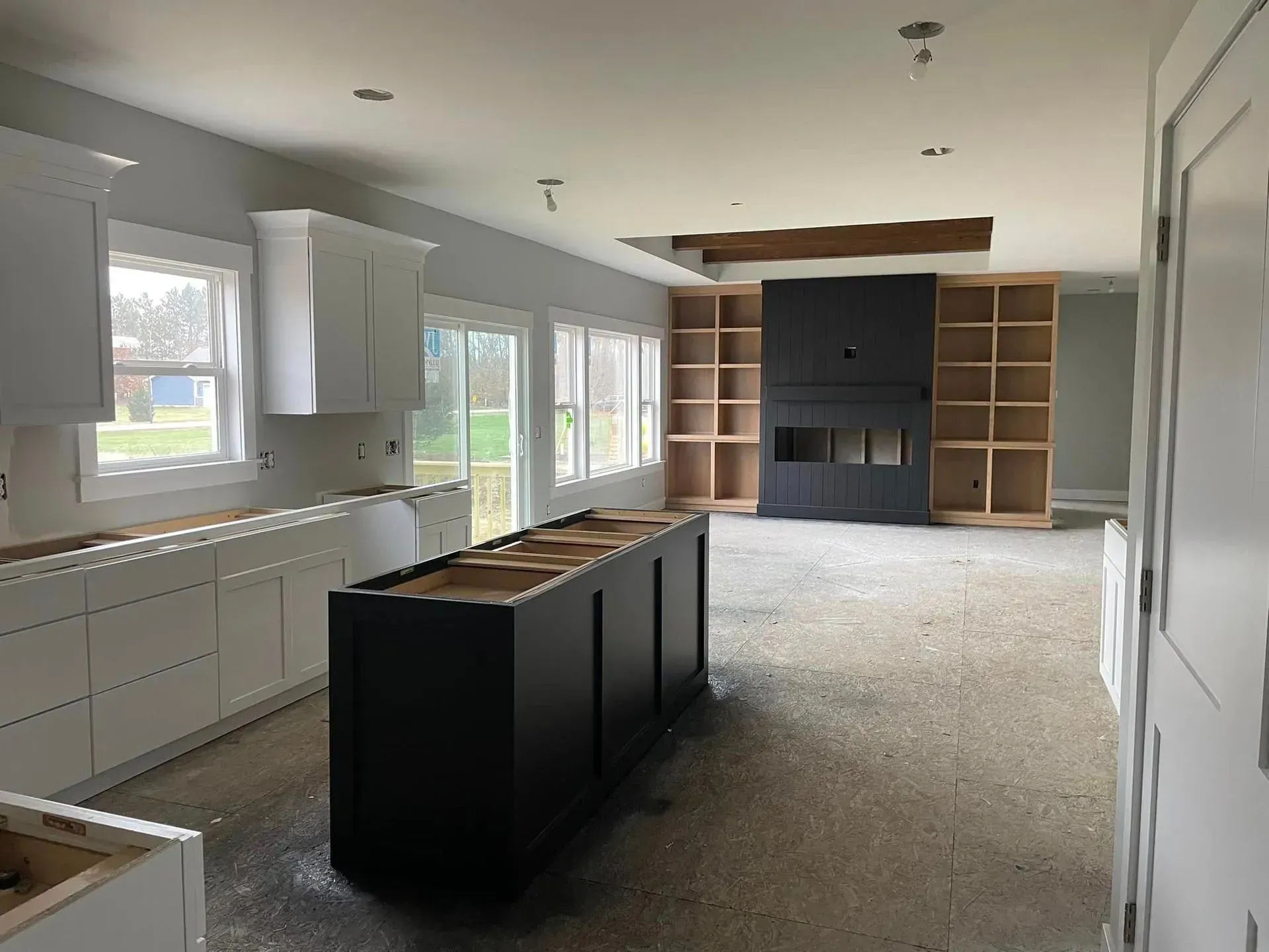 Modern kitchen under renovation with white cabinets, black island, and built-in shelving on the far wall