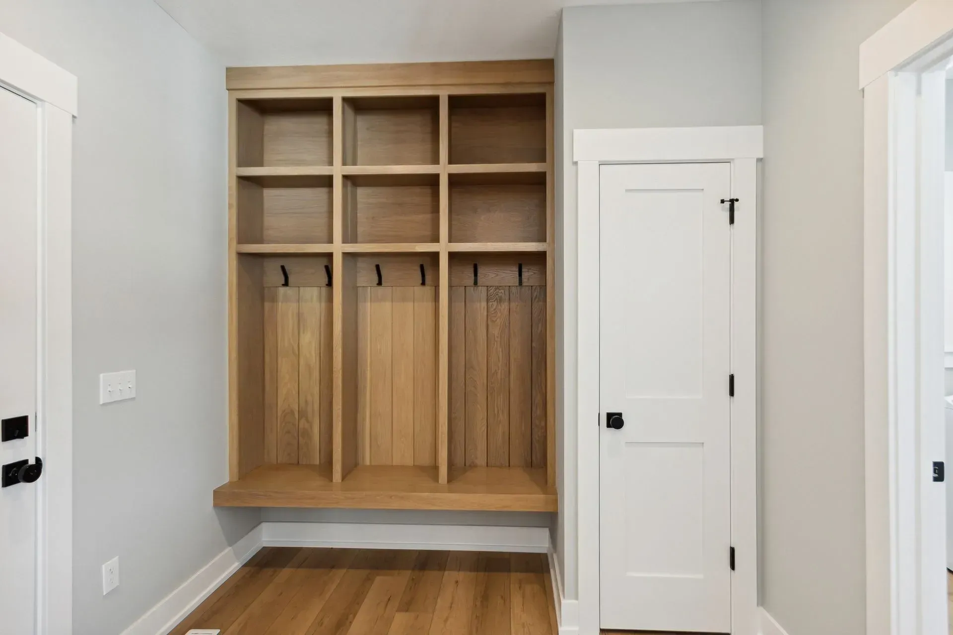 Built-in wooden locker cubbies in a bright hallway with white doors and hardwood floors