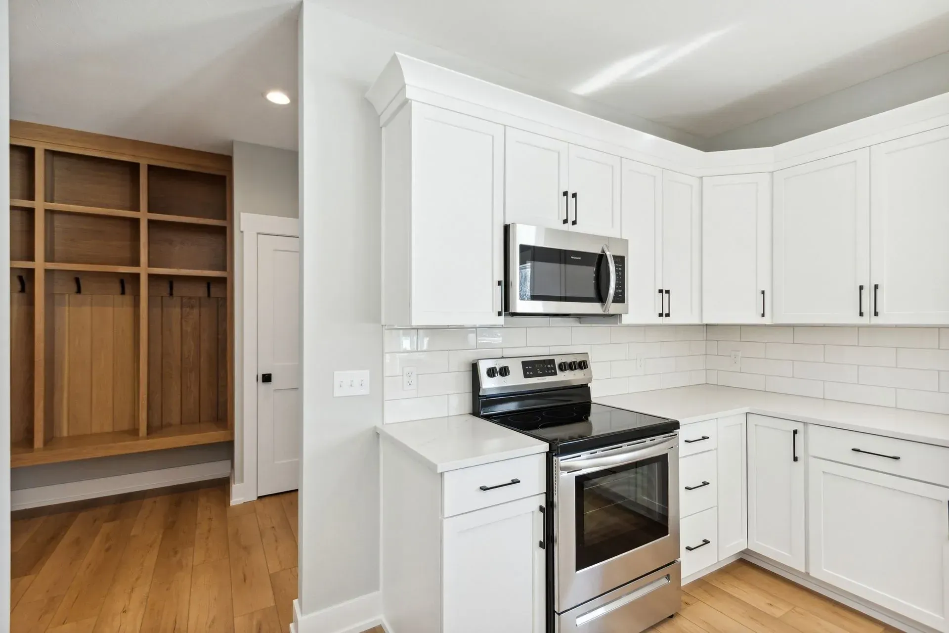Bright white kitchen with stainless steel stove, microwave, and built-in wooden closet nearby.