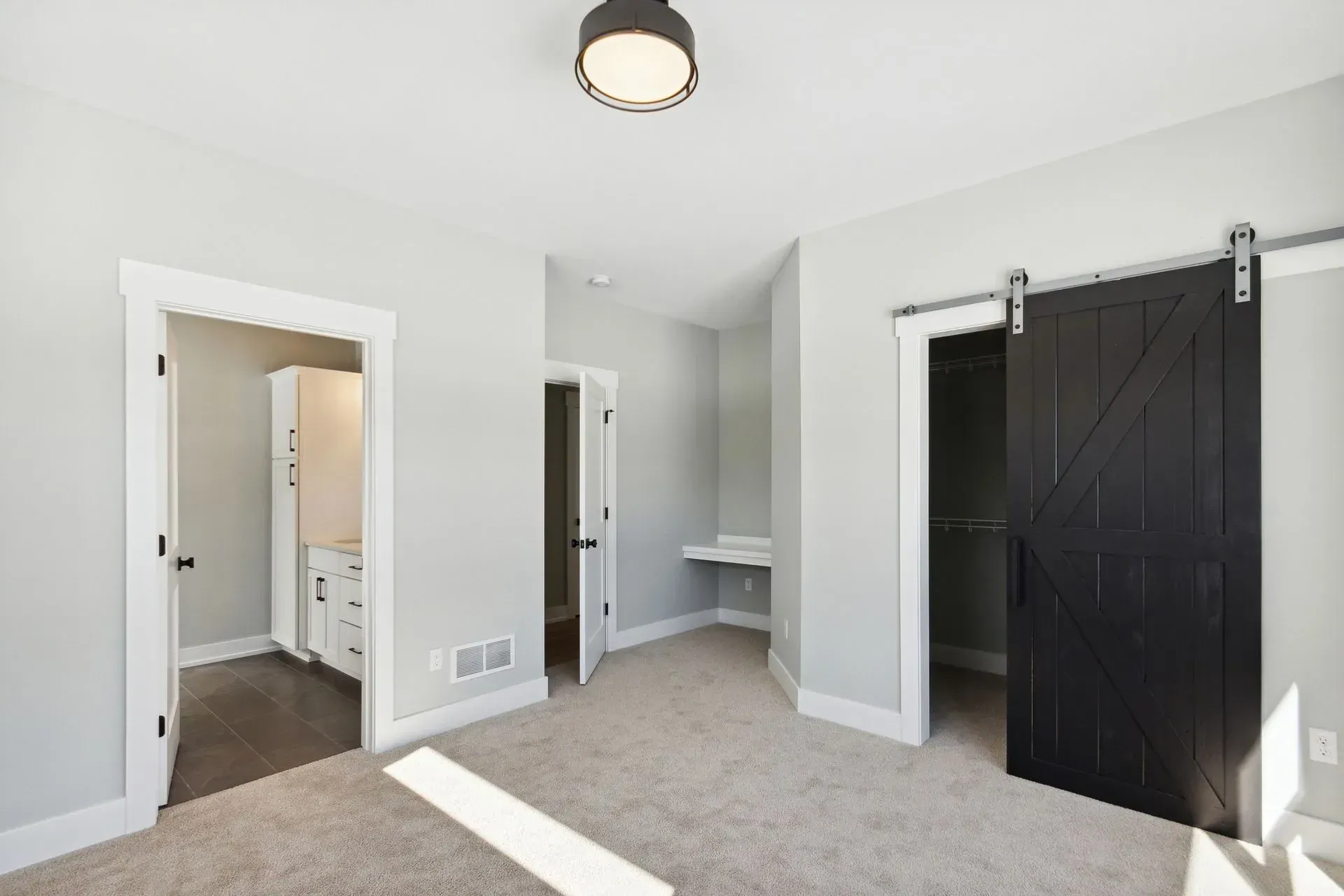Bright bedroom with carpet, white walls, open closet, and black barn door on the right
