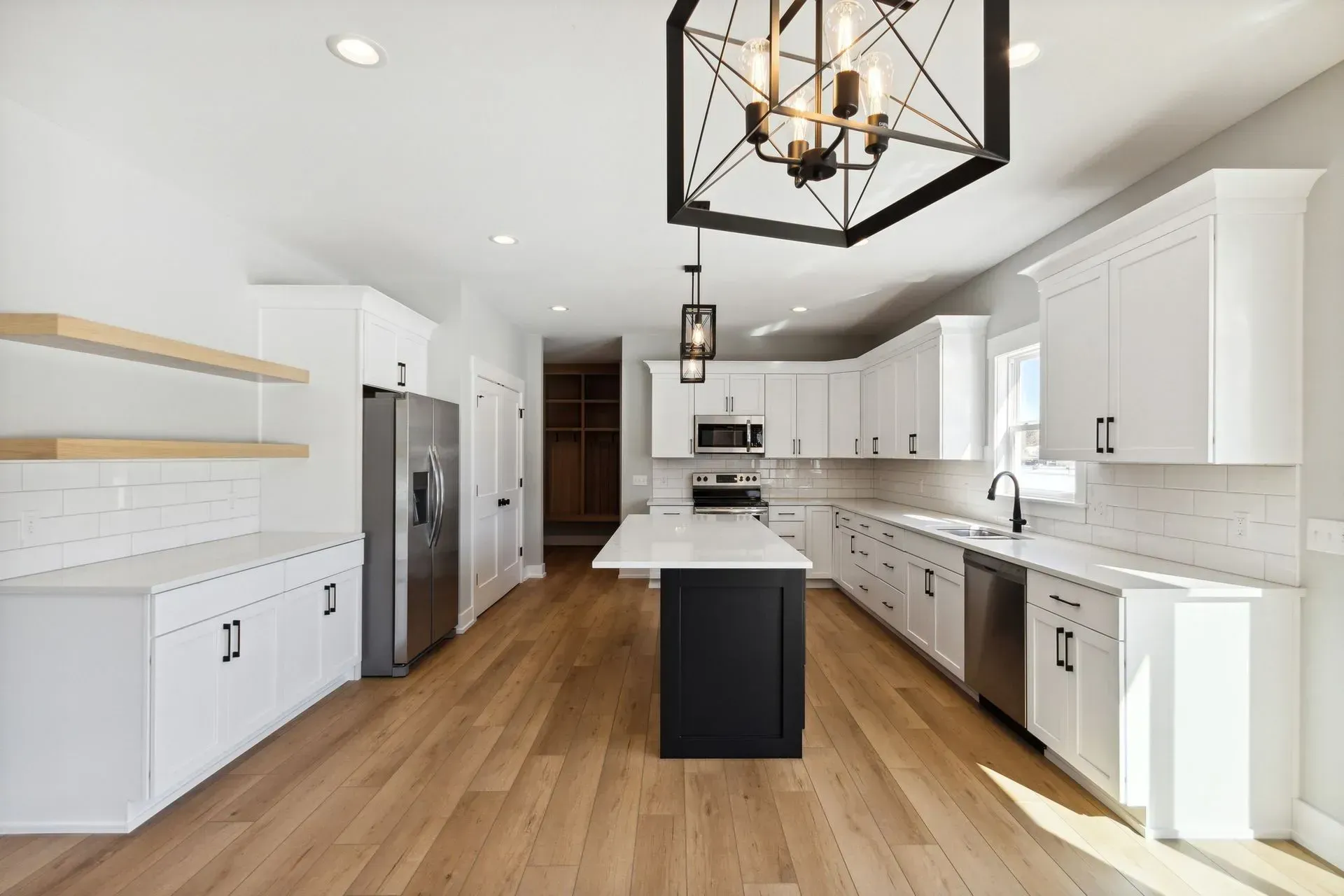 Bright modern kitchen with white cabinets, wood floors, stainless steel appliances, and a black island.
