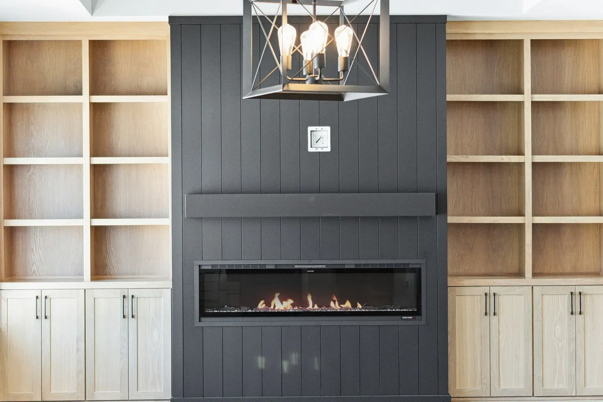 Modern built-in fireplace with black accent wall, white shelving, and a hanging lantern light
