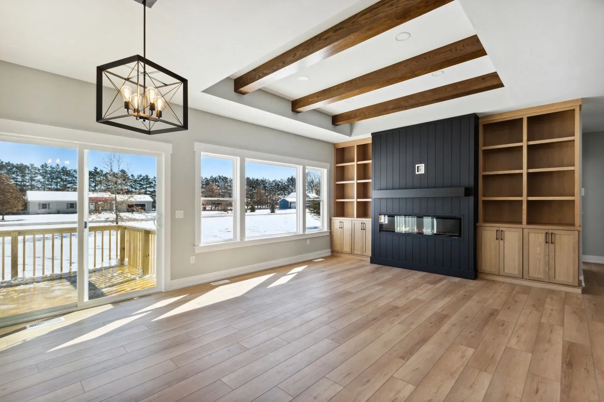 Bright modern living room with wood beams, large windows, fireplace, and built-in shelves.