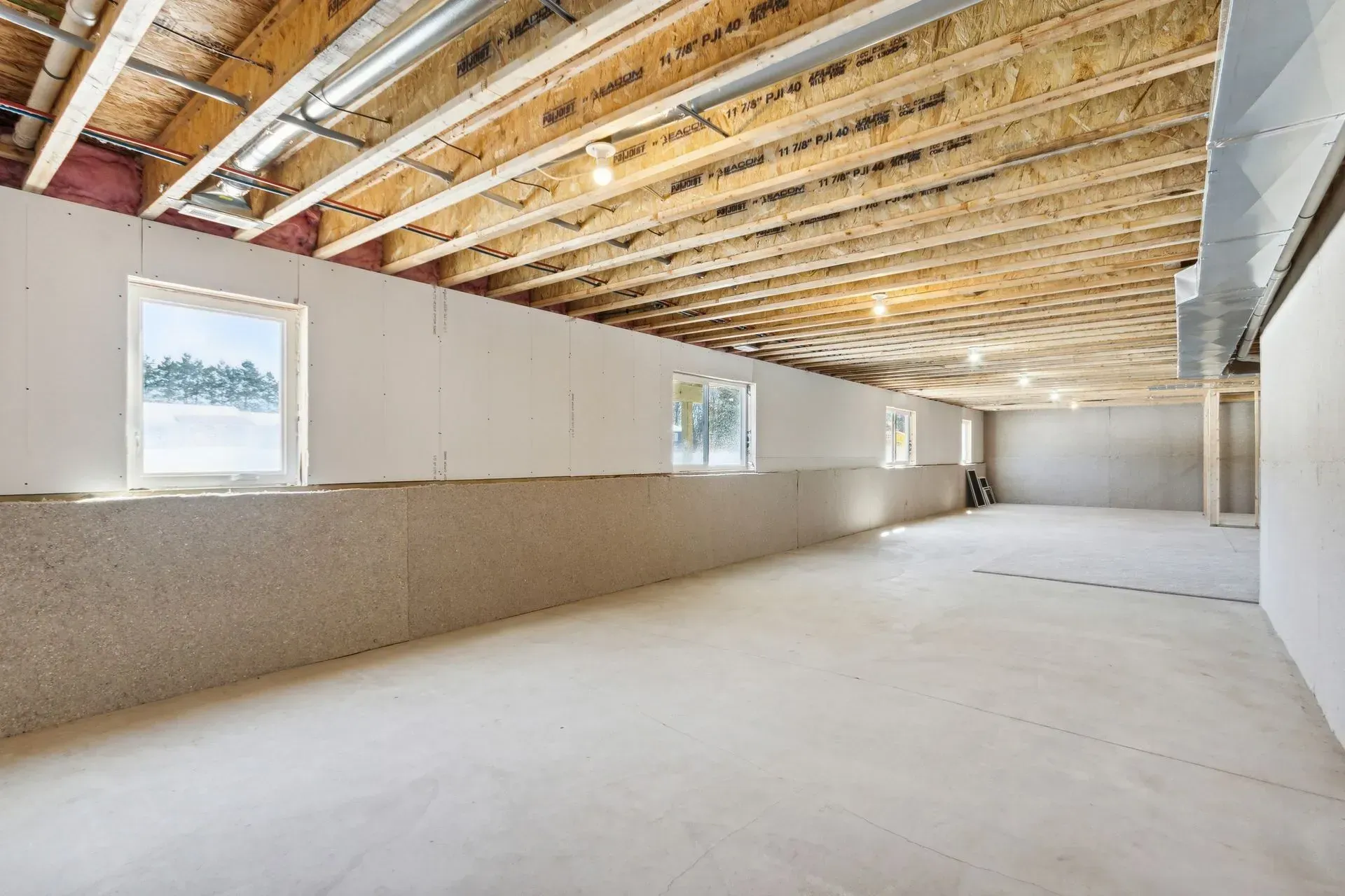 Empty unfinished basement with exposed ceiling joists, concrete floor, and small windows.