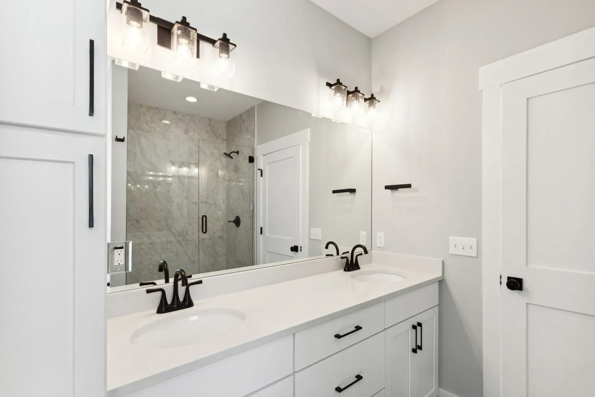 Modern white bathroom with large mirror, vanity, glass shower, and wall sconces