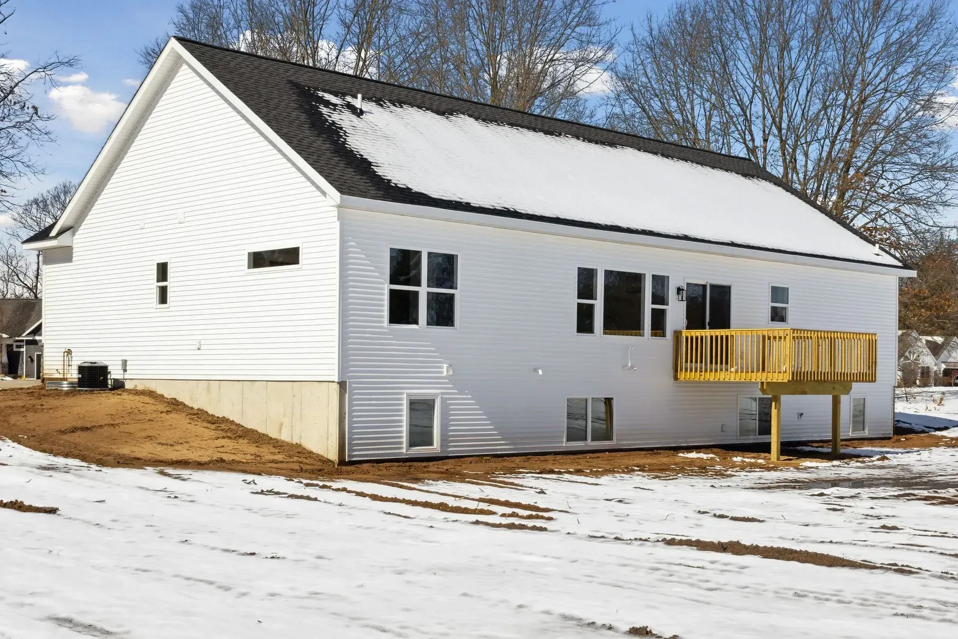 White house with snow-covered roof and yard, featuring a small yellow deck on the side