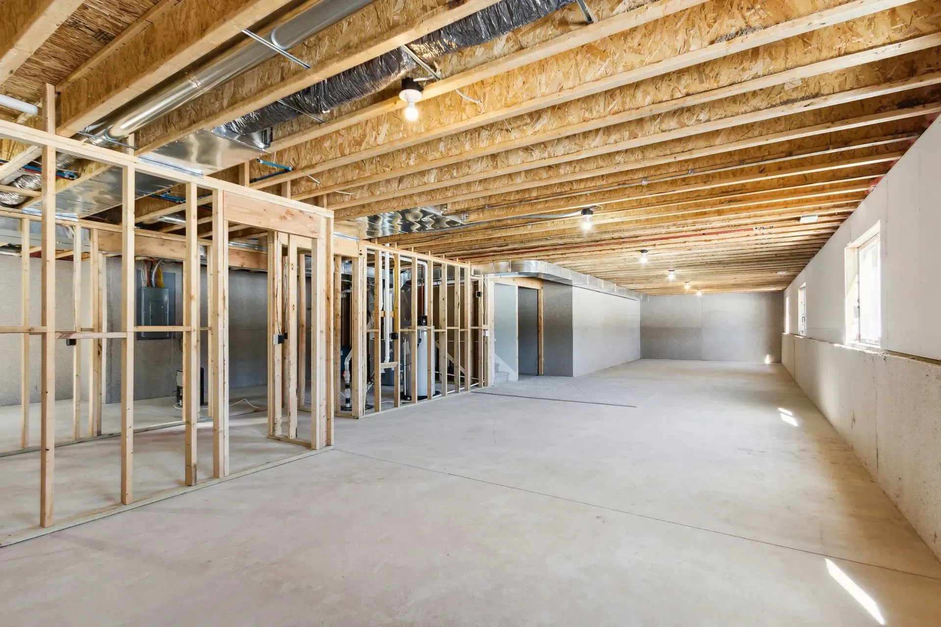 Empty unfinished basement with exposed wood framing, concrete floor, and daylight from windows
