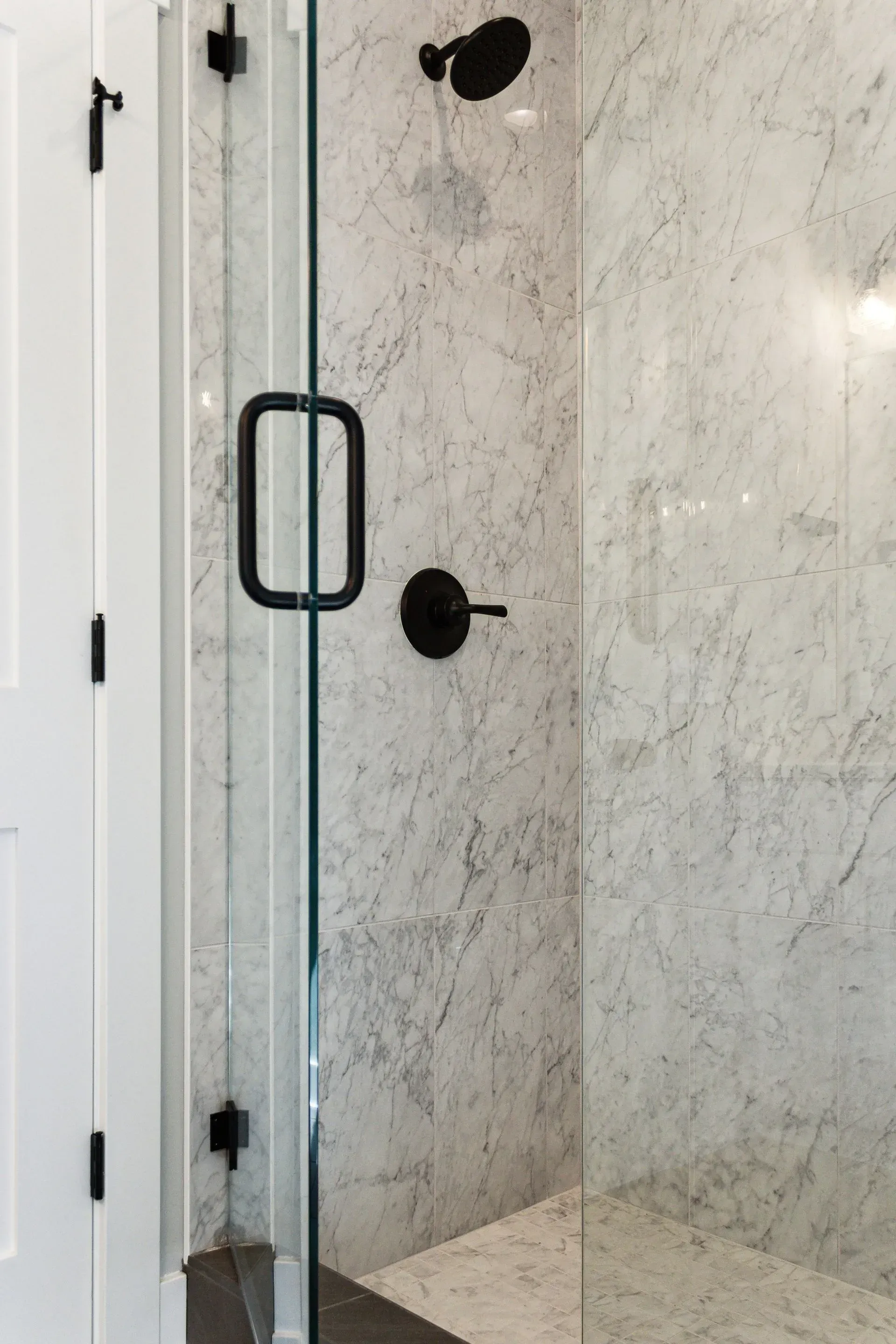Glass shower door with black handle and hinges beside marble-tile walls