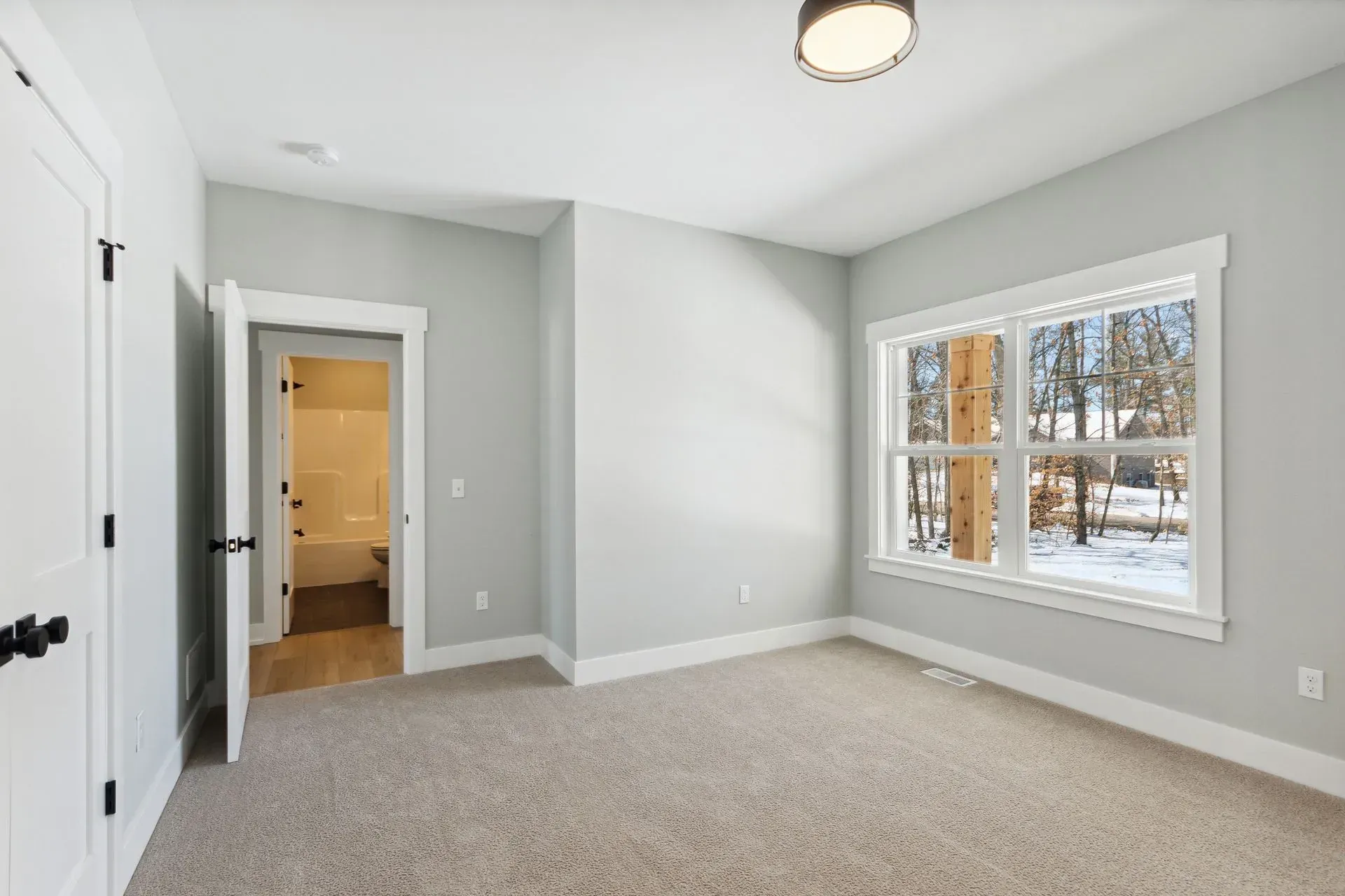 Empty beige bedroom with gray walls, carpet, and a window with white trim.