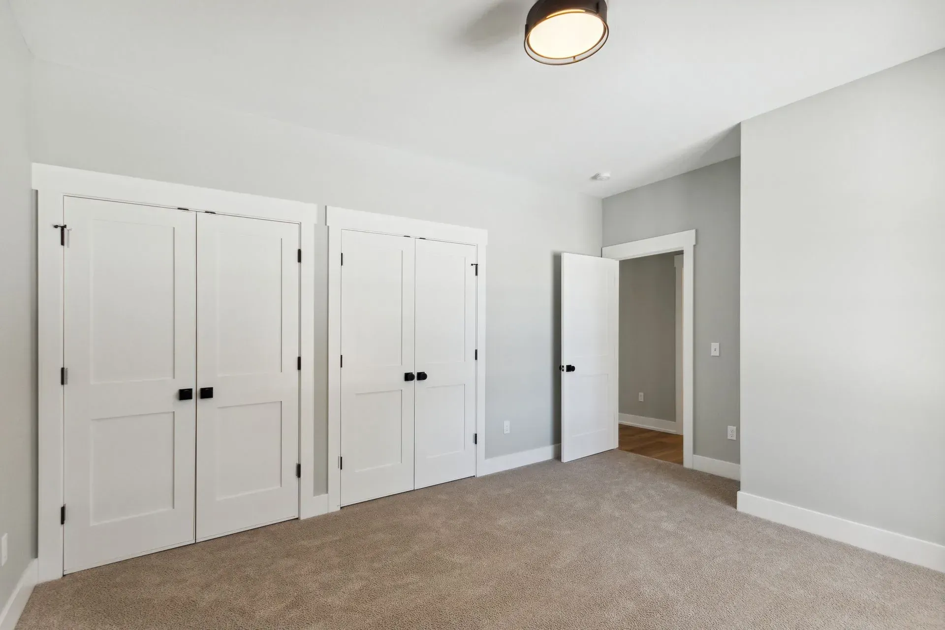 Empty carpeted bedroom with white double closet doors and an open doorway to a hall