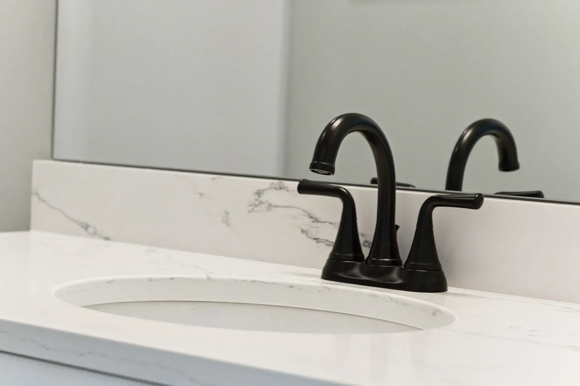 Black double-handle bathroom faucet on a white marble sink countertop with mirror reflection