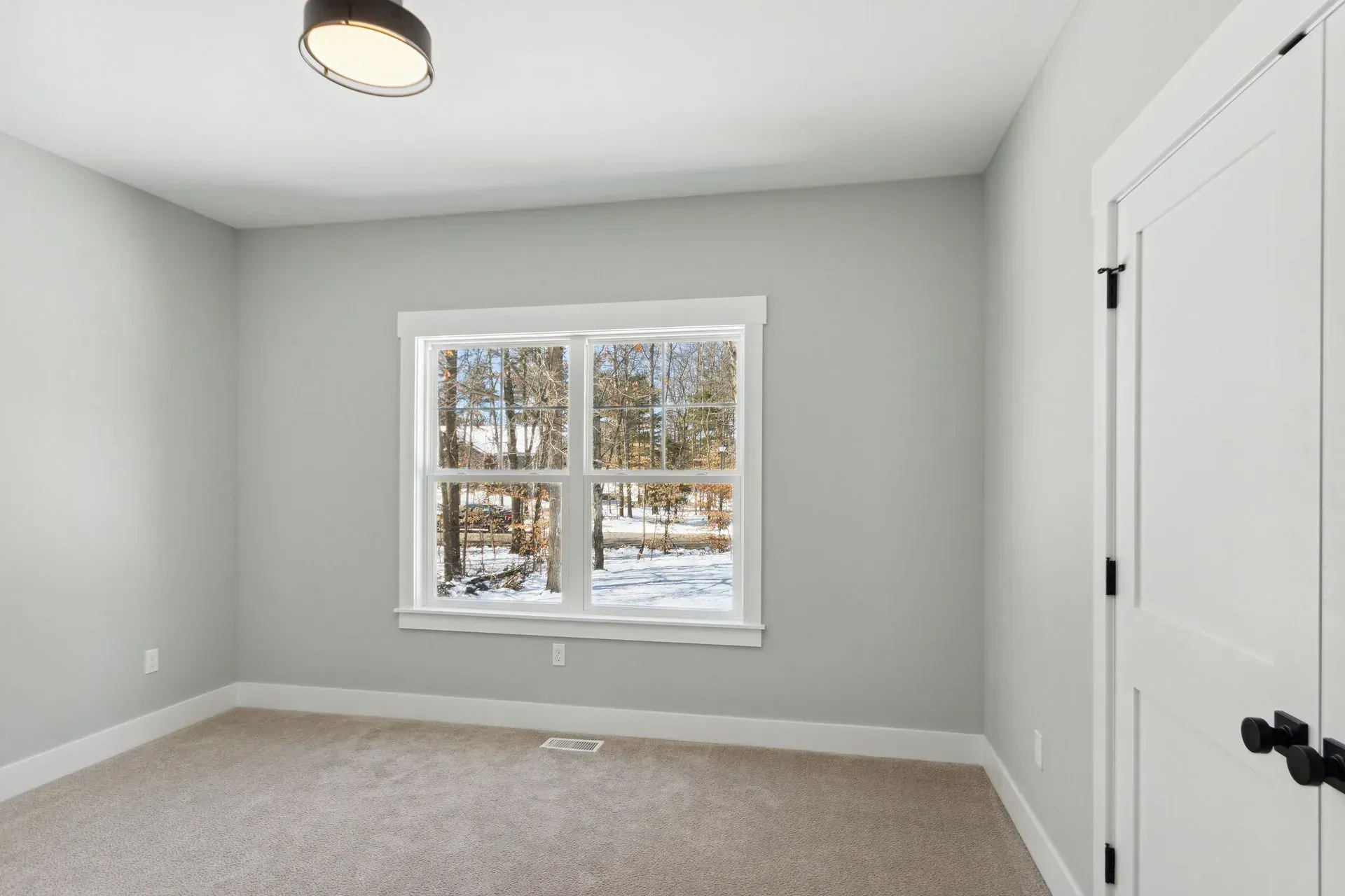 Empty gray bedroom with carpet, a window showing snowy trees, and a white closet door.