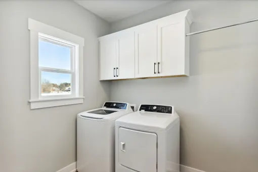 Laundry room with white cabinets, a window, and a washer and dryer against light gray walls