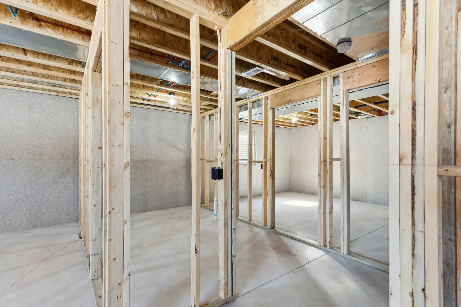Unfinished basement framing with exposed wood studs, beams, and concrete walls.