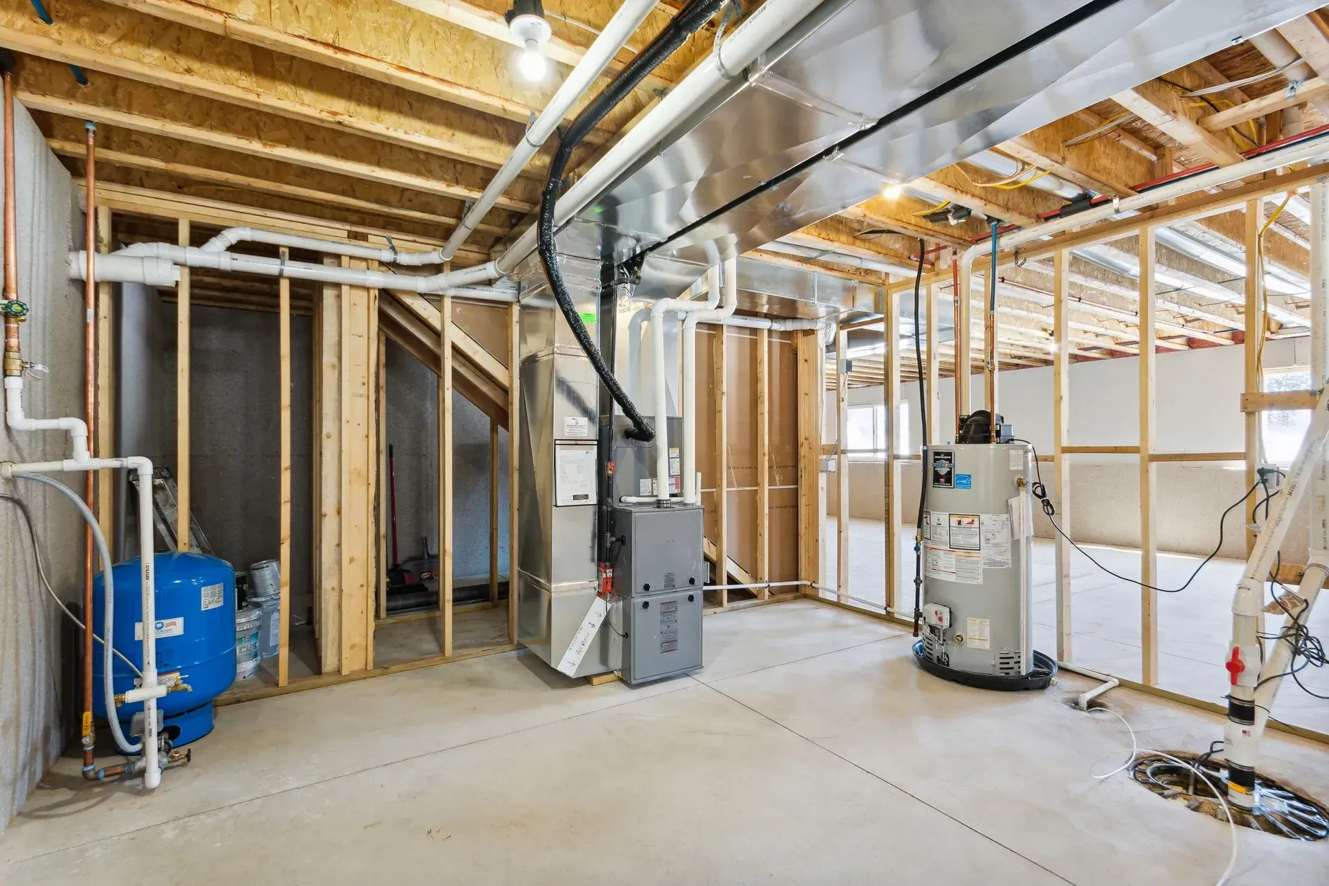 Unfinished basement with exposed framing, HVAC ducting, water heater, and concrete floor