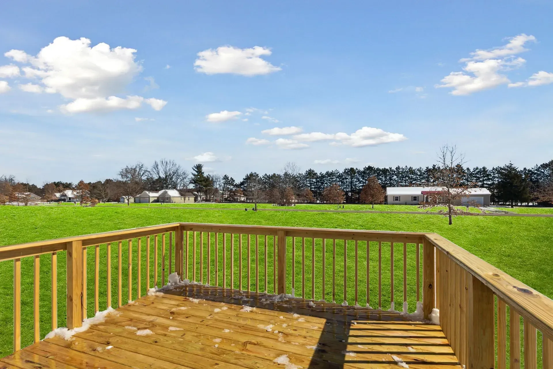 Wooden deck overlooking a green field under a blue sky with scattered clouds